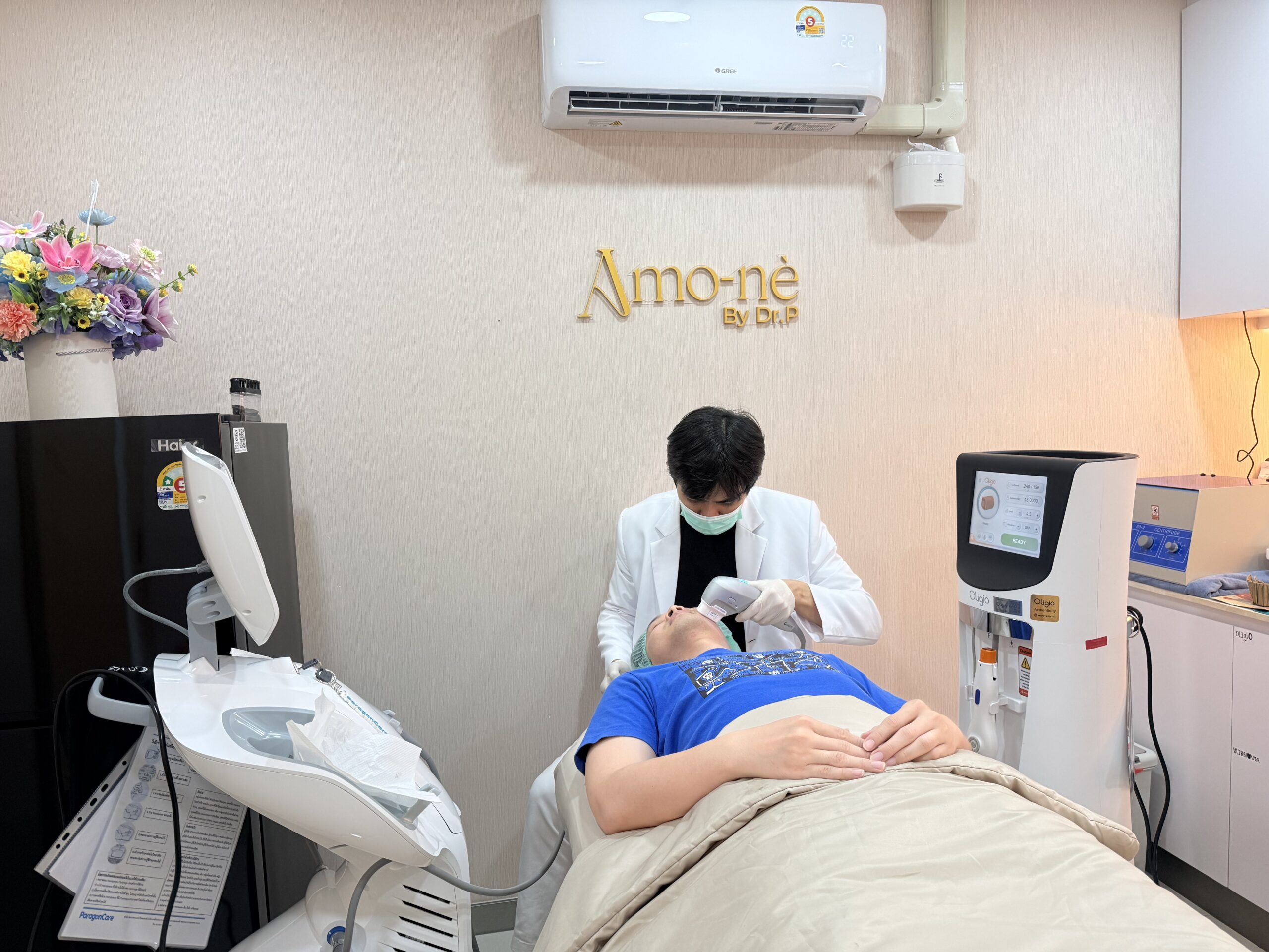 คลินิกความงาม Amo-nè By Dr.P แพทย์กำลังทำหัตถการเลเซอร์บนใบหน้าของผู้รับบริการที่นอนบนเตียง พร้อมเครื่องมือทางการแพทย์รอบข้าง