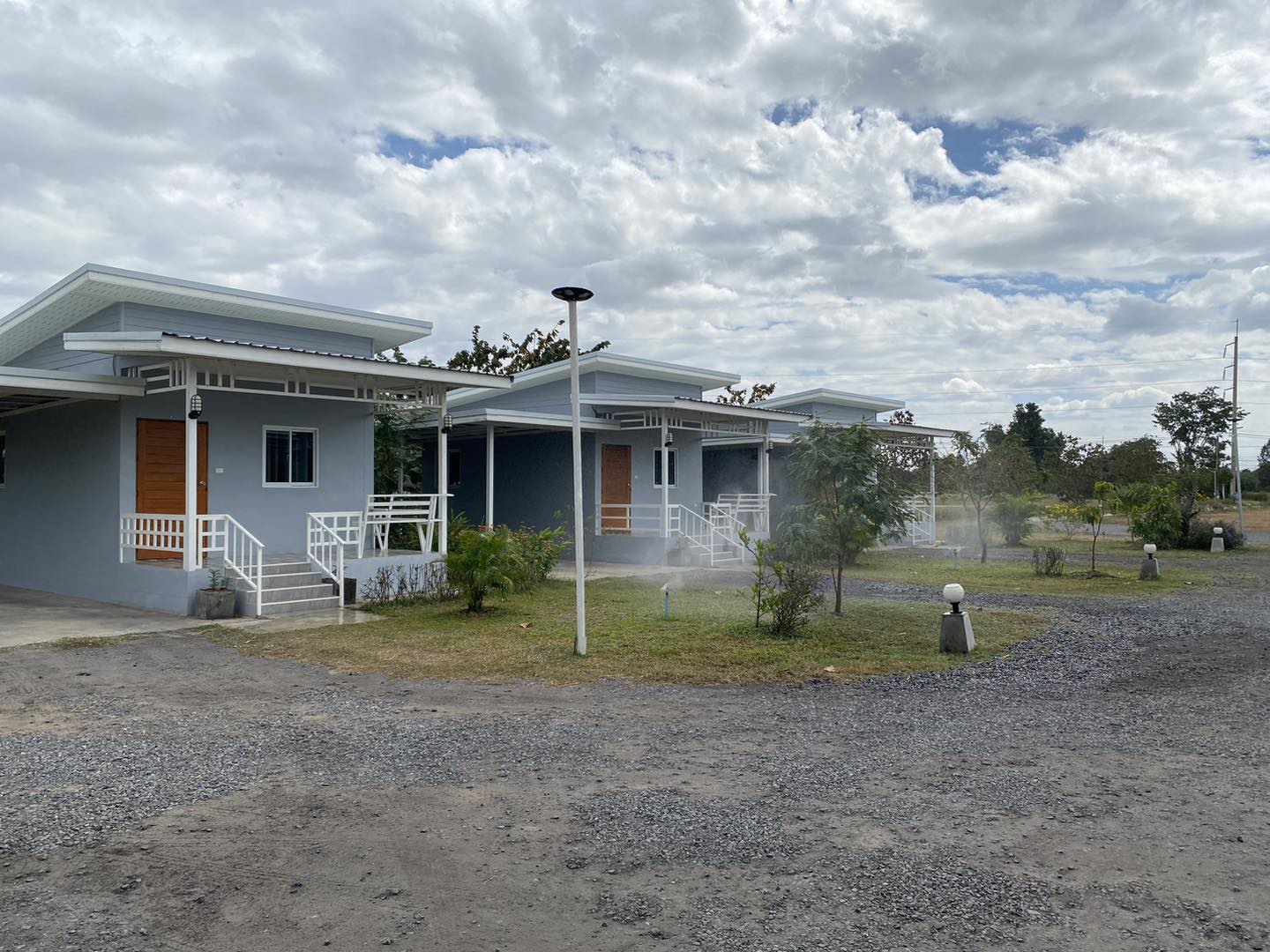 บังกะโลสีฟ้าหลายหลังพร้อมบันไดสีขาวและประตูไม้สีน้ำตาล ล้อมรอบด้วยสนามหญ้าและต้นไม้