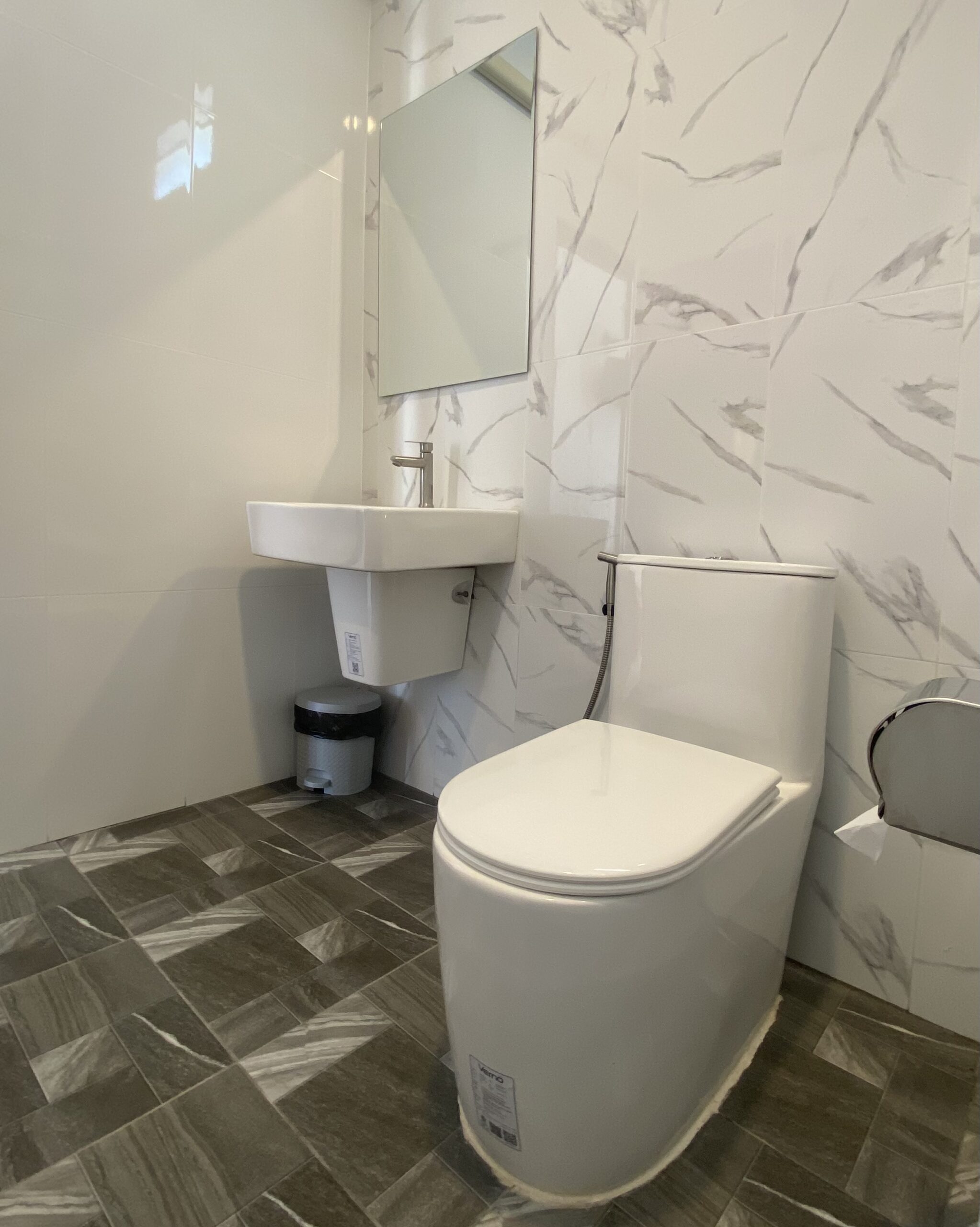 ห้องน้ำสะอาดตกแต่งด้วยกระเบื้องลายหินอ่อนสีขาว มีโถสุขภัณฑ์ อ่างล้างมือ และกระจก