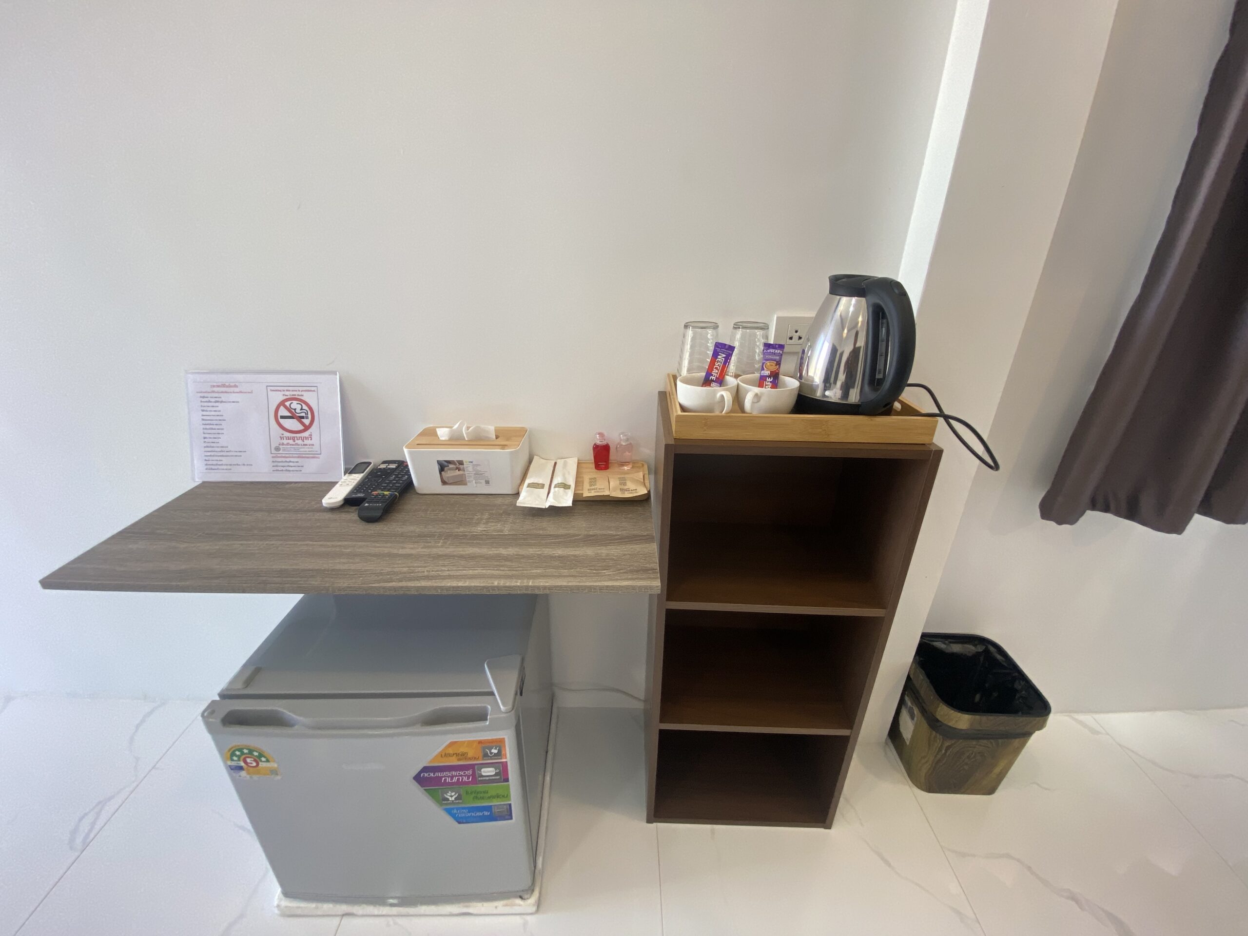 มุมเครื่องดื่มในห้องพักโรงแรม มีตู้เย็นมินิบาร์ กาต้มน้ำไฟฟ้า แก้วน้ำ ถาดชา-กาแฟ รีโมททีวี และป้ายห้ามสูบบุหรี่