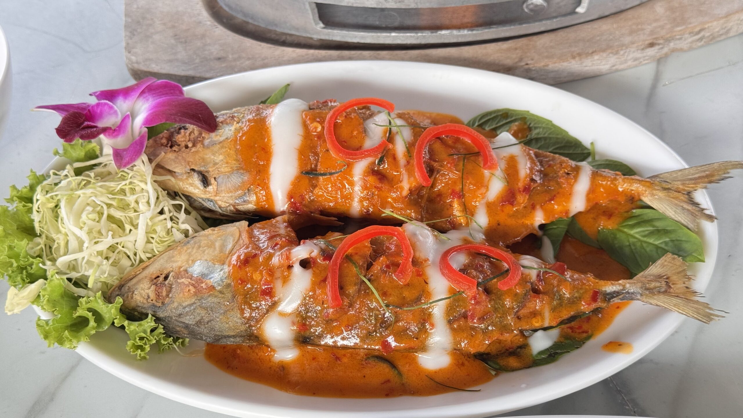 ปลาทูทอดราดพริกแกงเผ็ดกะทิ ตกแต่งด้วยพริกแดงและใบโหระพา เสิร์ฟบนจานขาวพร้อมผักสด