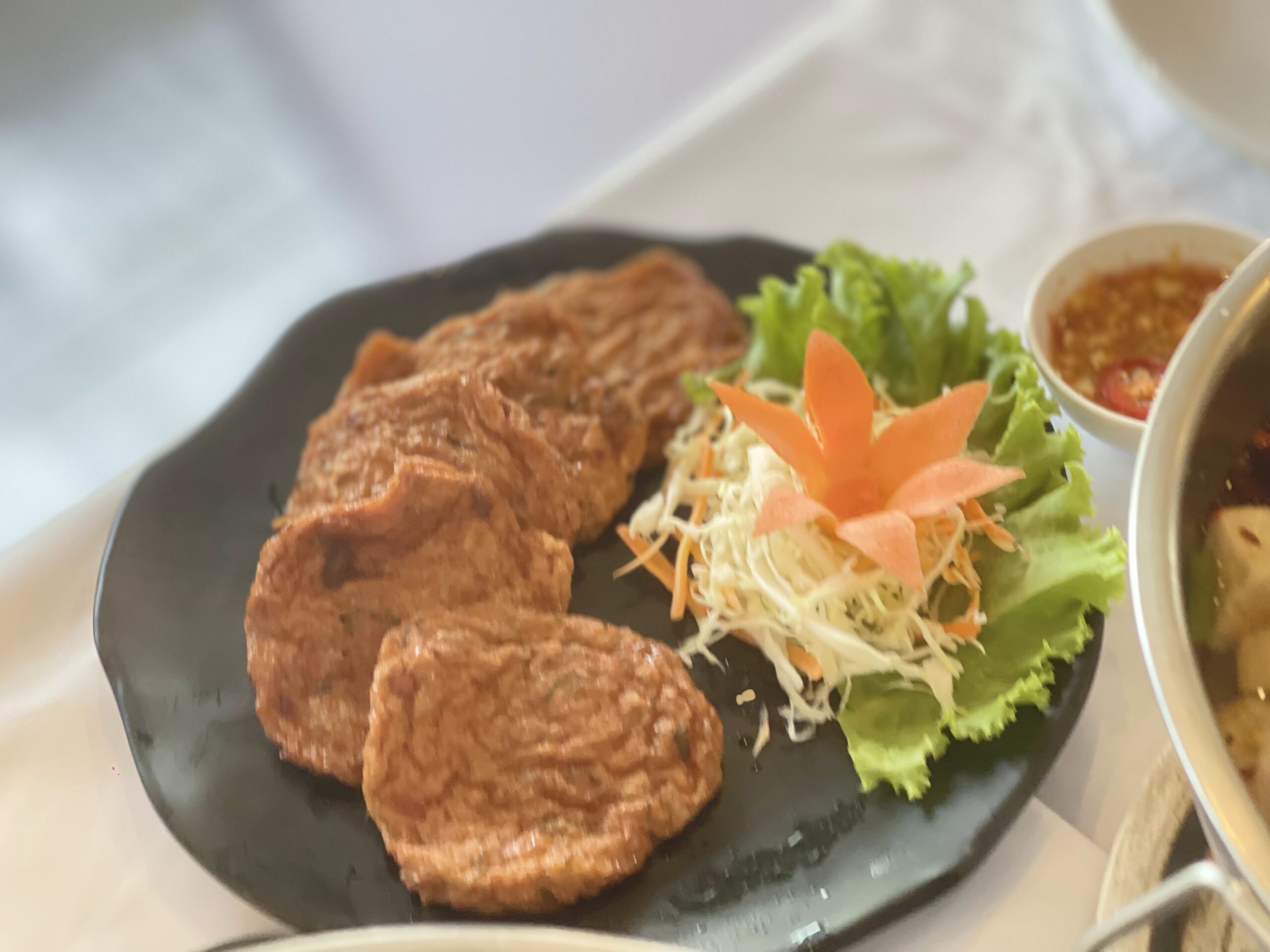 ทอดมันปลาทอดกรอบเสิร์ฟบนจานดำพร้อมผักสดแต่งจานและน้ำจิ้มรสเด็ด