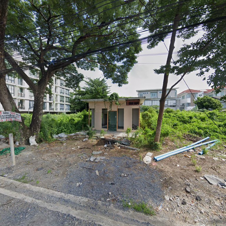 อาคารร้างกลางพุ่มไม้รกครึ้มริมถนน มีท่อน้ำสีฟ้าวางอยู่ข้างๆ และคอนโดมิเนียมอยู่ด้านหลัง