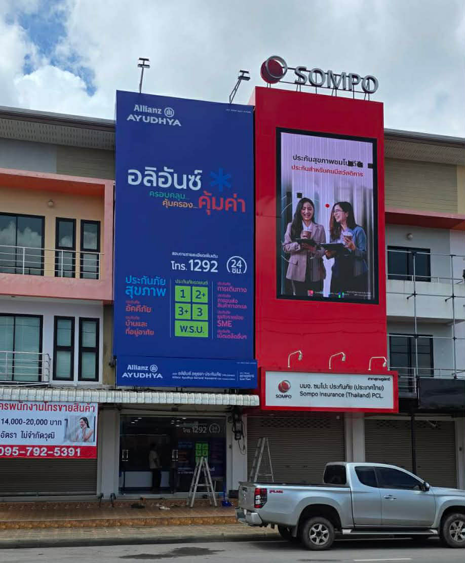 อาคารสำนักงานประกันภัยอลิอันซ์อยุธยาและซมโปะ ประเทศไทย พร้อมป้ายโฆษณาขนาดใหญ่และรถกระบะจอดอยู่ด้านหน้า