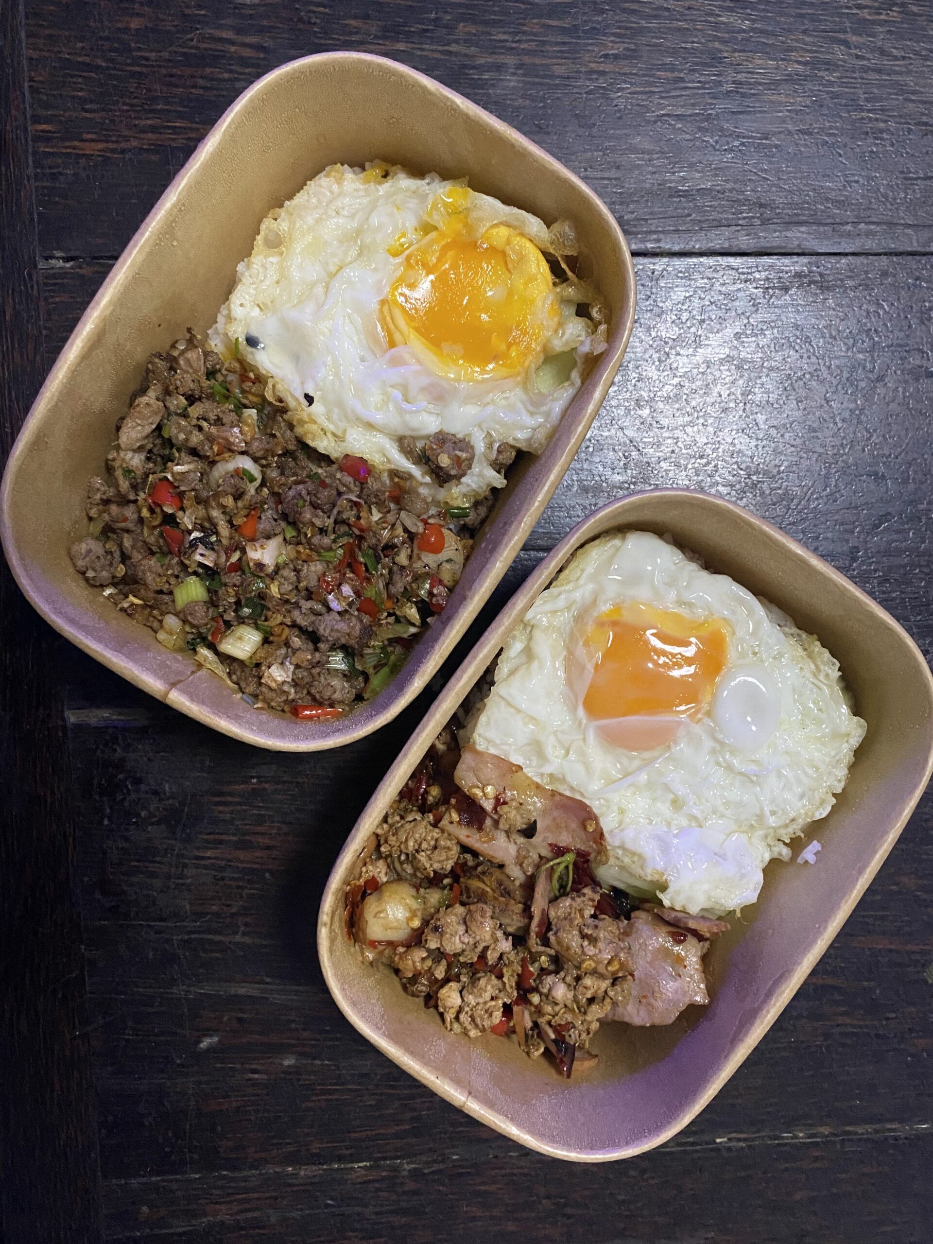 กะเพราสับ 2 กล่องพร้อมไข่ดาว เสิร์ฟในกล่องกระดาษบนโต๊ะไม้เข้ม