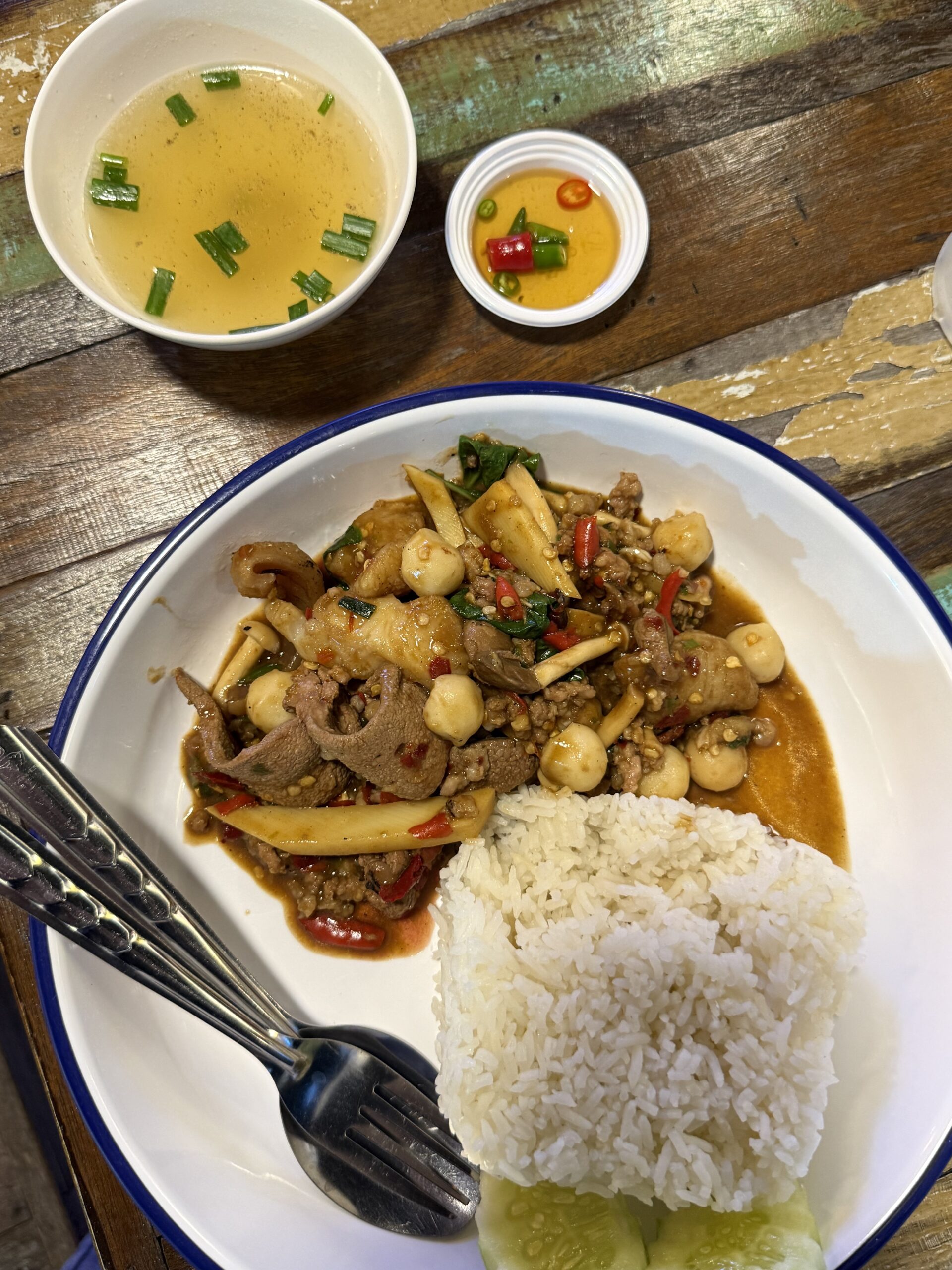 ข้าวราดผัดกะเพราเนื้อใส่เห็ดและพริก เสิร์ฟพร้อมข้าวสวย แตงกวา น้ำซุป และน้ำปลาพริก บนโต๊ะไม้