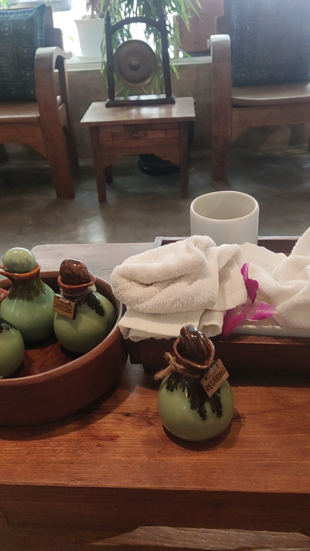 ขวดน้ำมันอโรมาเทอราพีเซรามิกสีเขียวพร้อมผ้าขนหนูสีขาวและดอกกล้วยไม้สีชมพูบนถาดไม้ในสปา