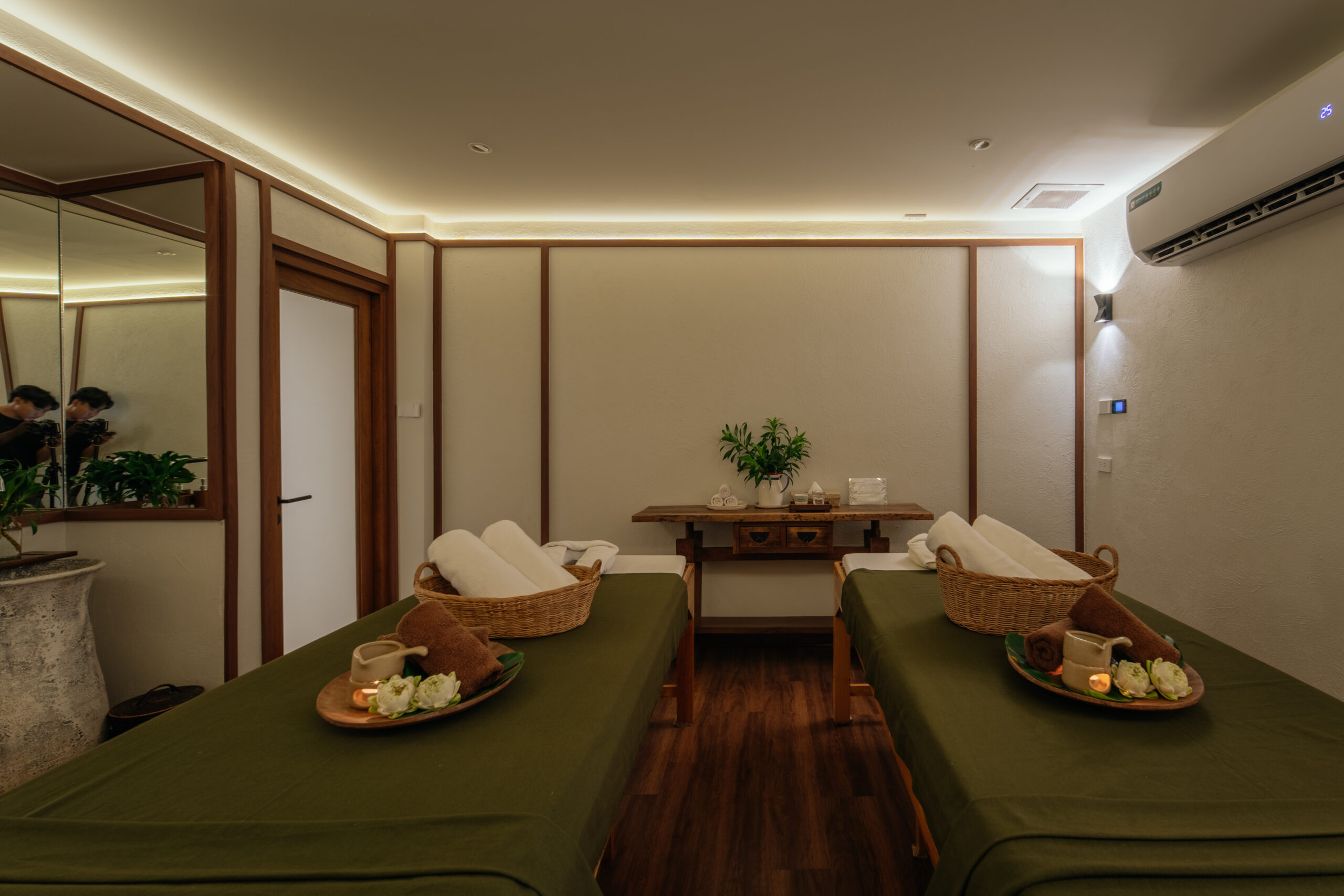 ห้องสปานวดคู่ตกแต่งหรูหราพร้อมเตียงนวดสองเตียงคลุมผ้าสีเขียว มีถาดดอกไม้และเทียนหอม บรรยากาศผ่อนคลาย