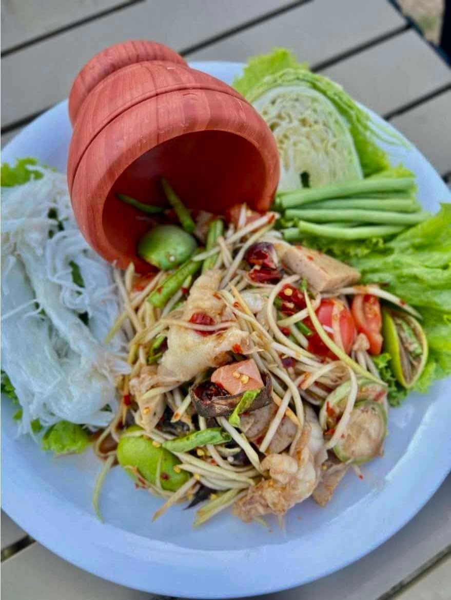 ส้มตำไทยจากครกดินเผา เสิร์ฟพร้อมขนมจีน ผักสด ถั่วฝักยาว กะหล่ำปลี บนจานขาว