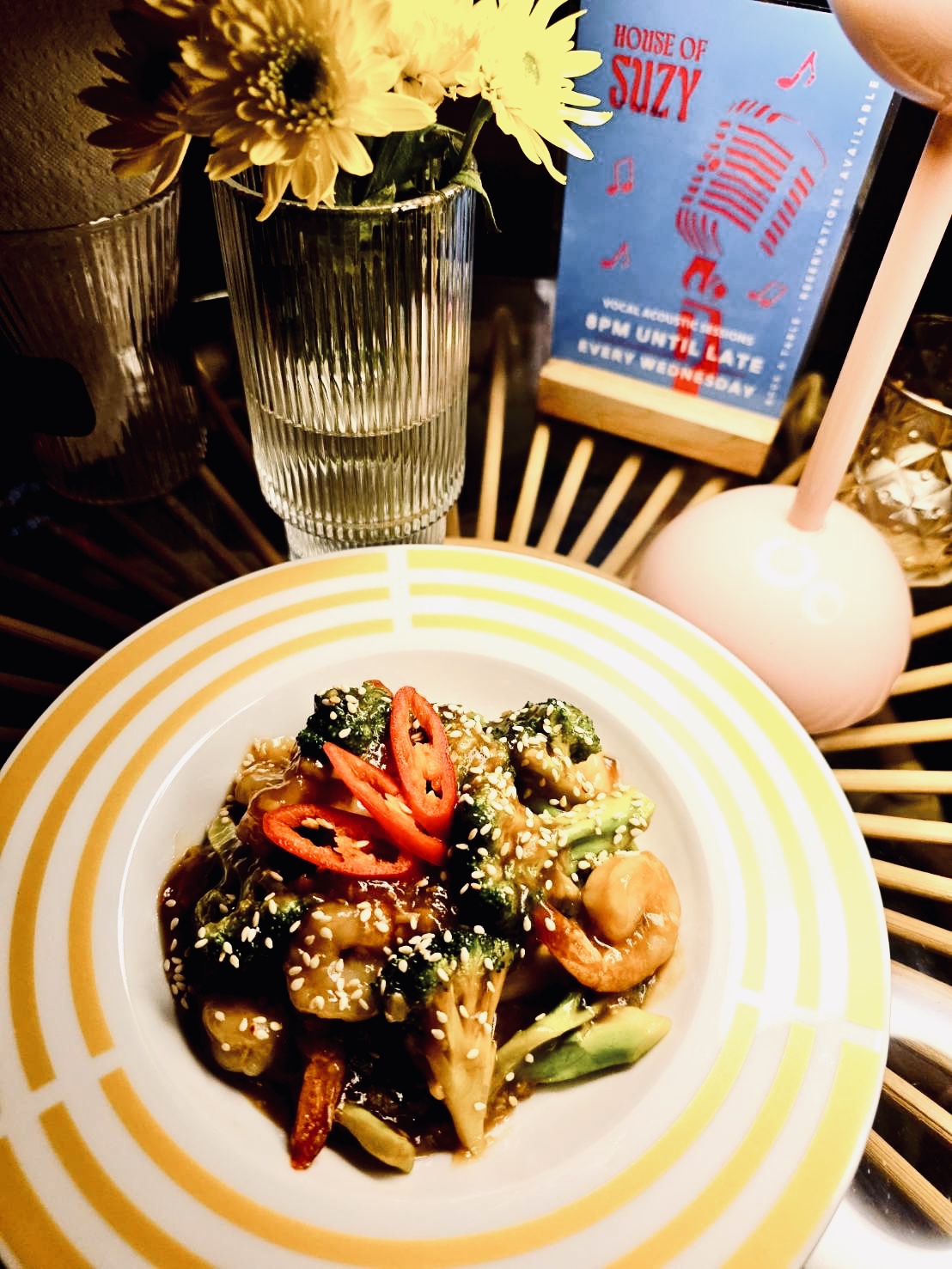 จานผัดบร็อคโคลี่กับเม็ดมะม่วงหิมพานต์ราดซอสสีน้ำตาล โรยงาขาวและพริกแดงสด เสิร์ฟบนจานลายทางสีเหลืองที่ร้าน House of Suzy