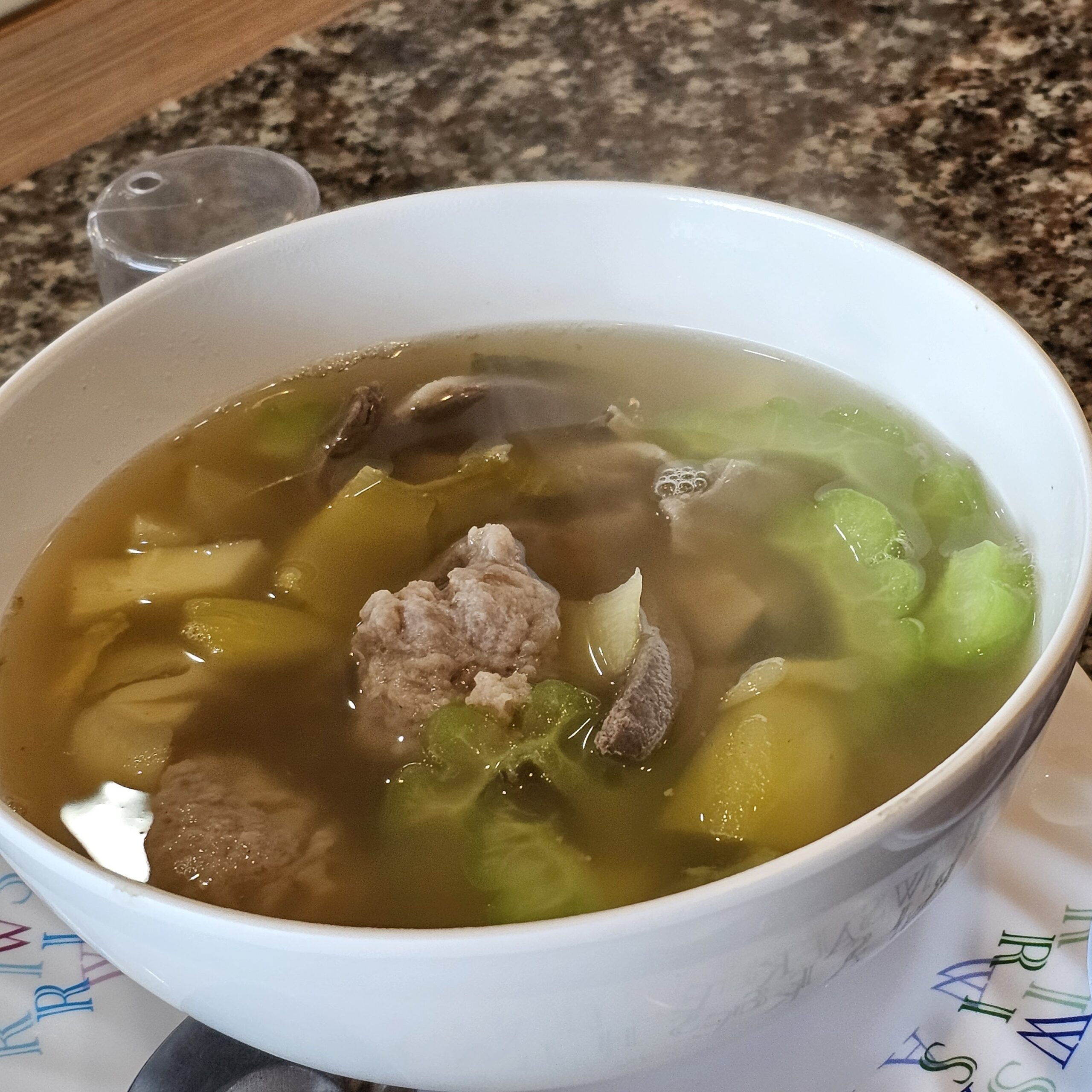 ชามซุปใสใส่ลูกชิ้นหมูสับ เห็ด และผักกาดเขียวในชามสีขาว