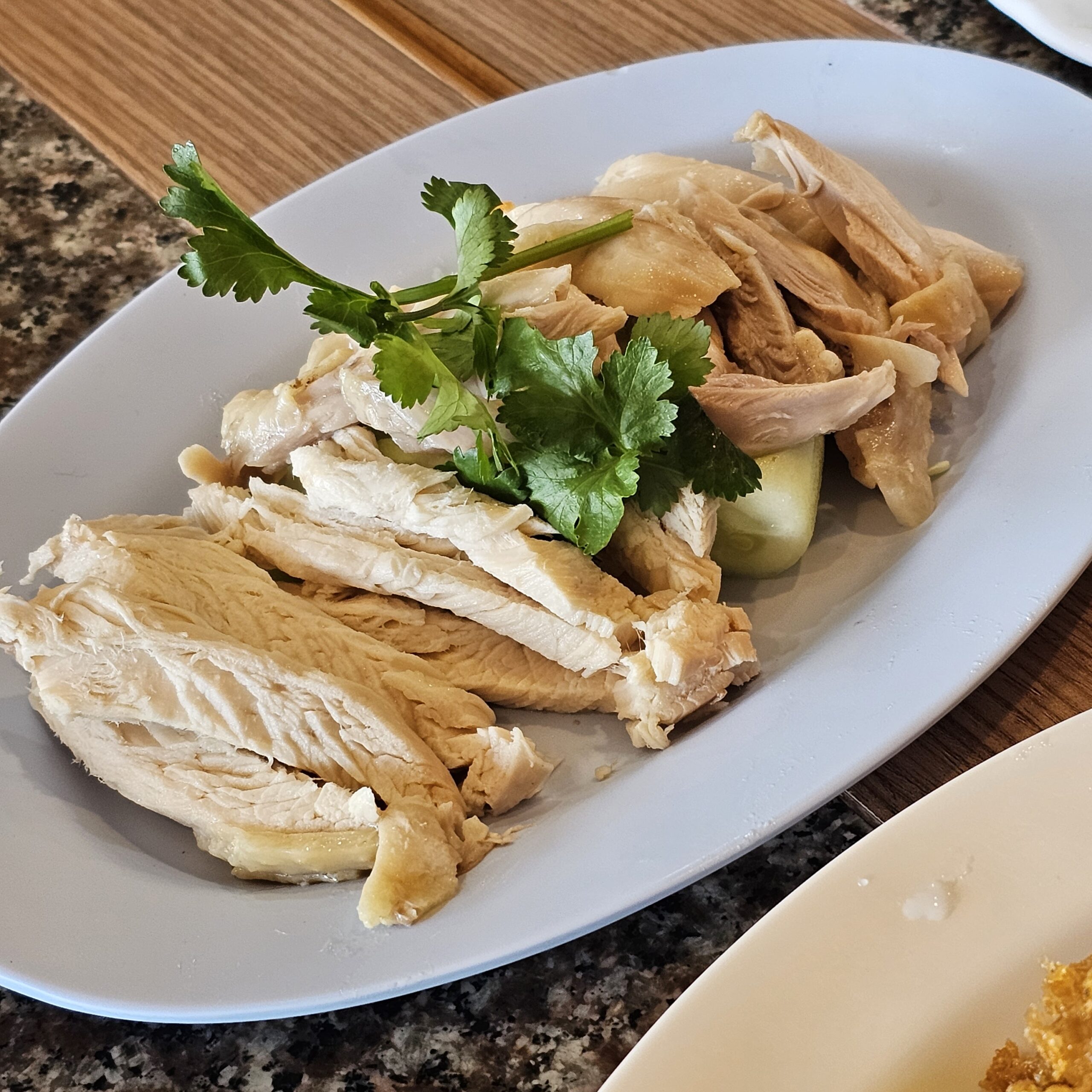 จานข้าวมันไก่ เนื้อไก่ต้มหั่นเป็นชิ้นเรียงสวยบนจานขาว ตกแต่งด้วยผักชีและแตงกวา