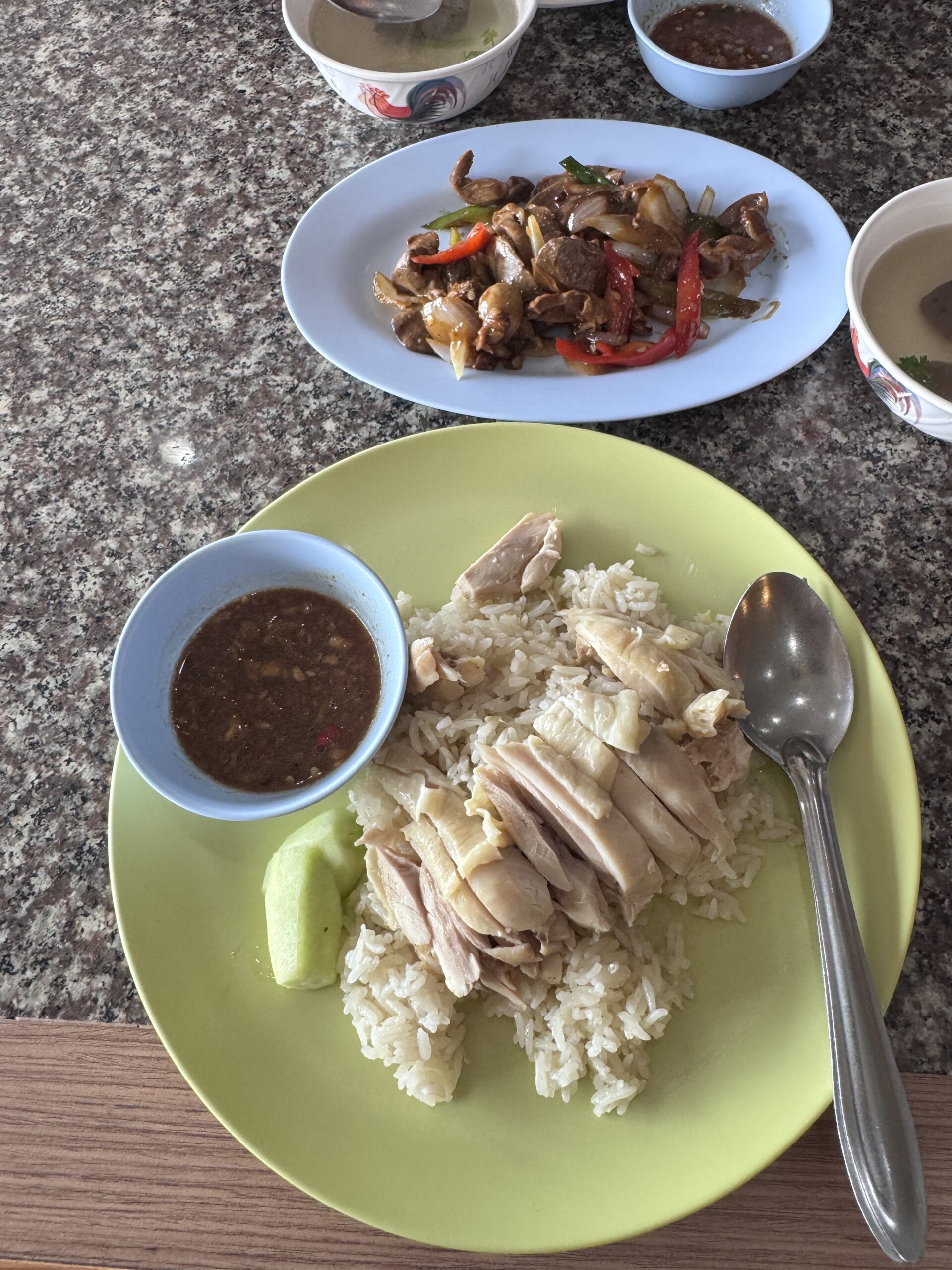 ข้าวมันไก่พร้อมน้ำจิ้มและแตงกวา เสิร์ฟคู่กับผัดเครื่องในไก่กับพริกหยวกบนโต๊ะหินอ่อน