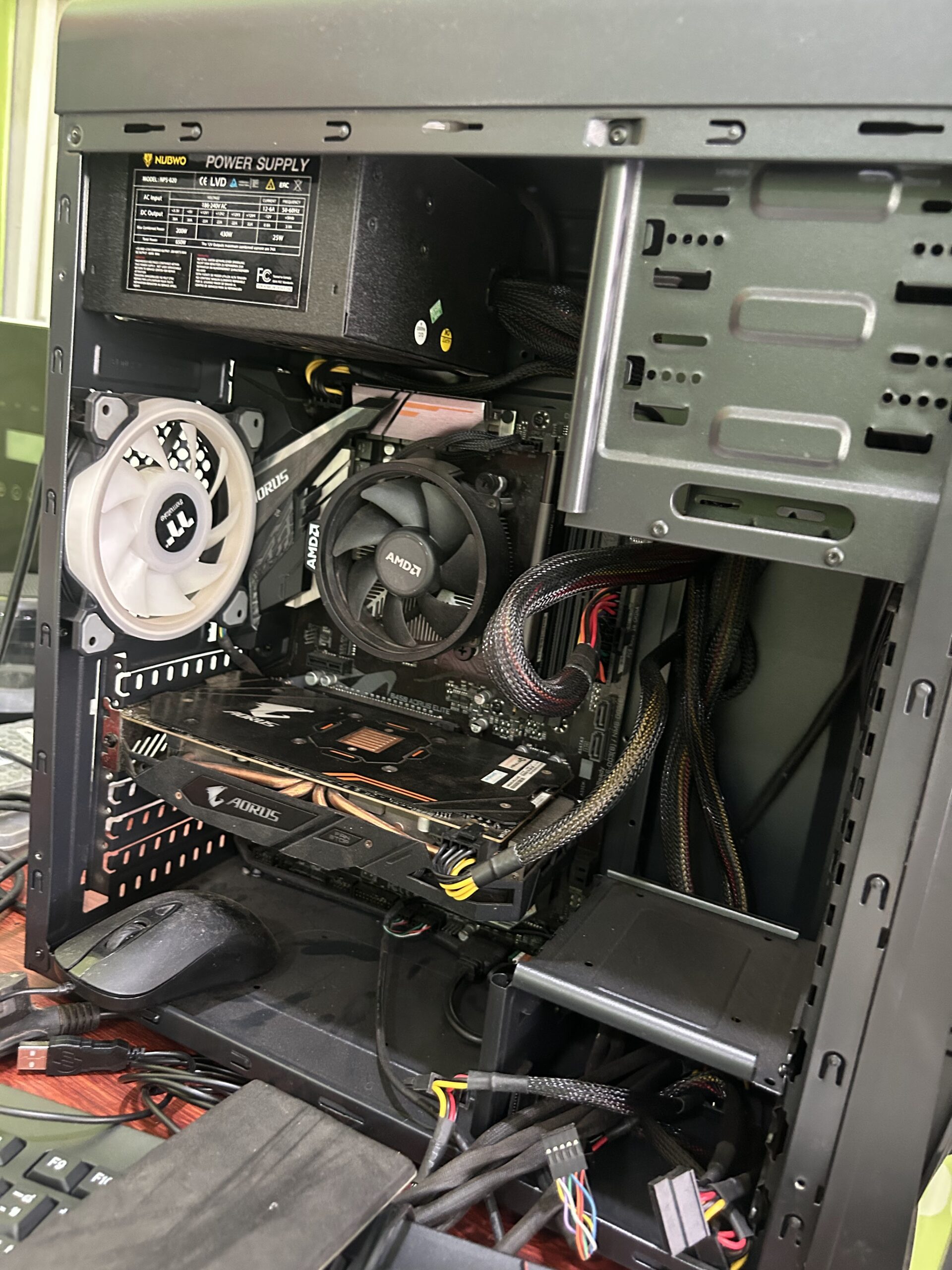 ภายในเคสคอมพิวเตอร์เดสก์ท็อปที่เปิดฝาออก แสดงพาวเวอร์ซัพพลาย NUBWO พัดลม AMD การ์ดจอ AORUS และสายเคเบิลต่างๆ