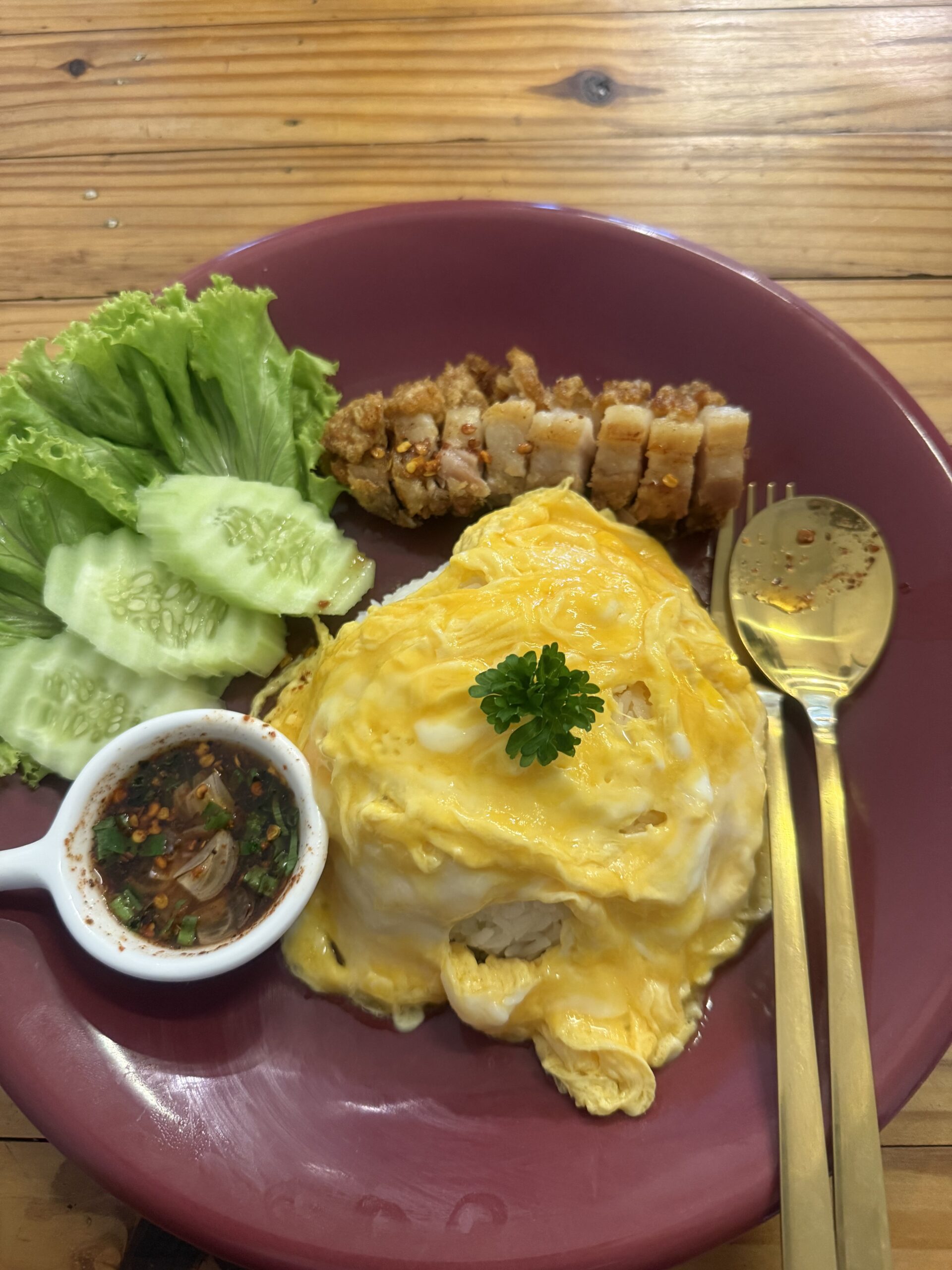 ข้ามไข่ข้นห่อข้าวพร้อมหมูกรอบหั่นชิ้น เสิร์ฟกับแตงกวา ผักกาดหอม และน้ำจิ้มแจ่วบนจานสีม่วง