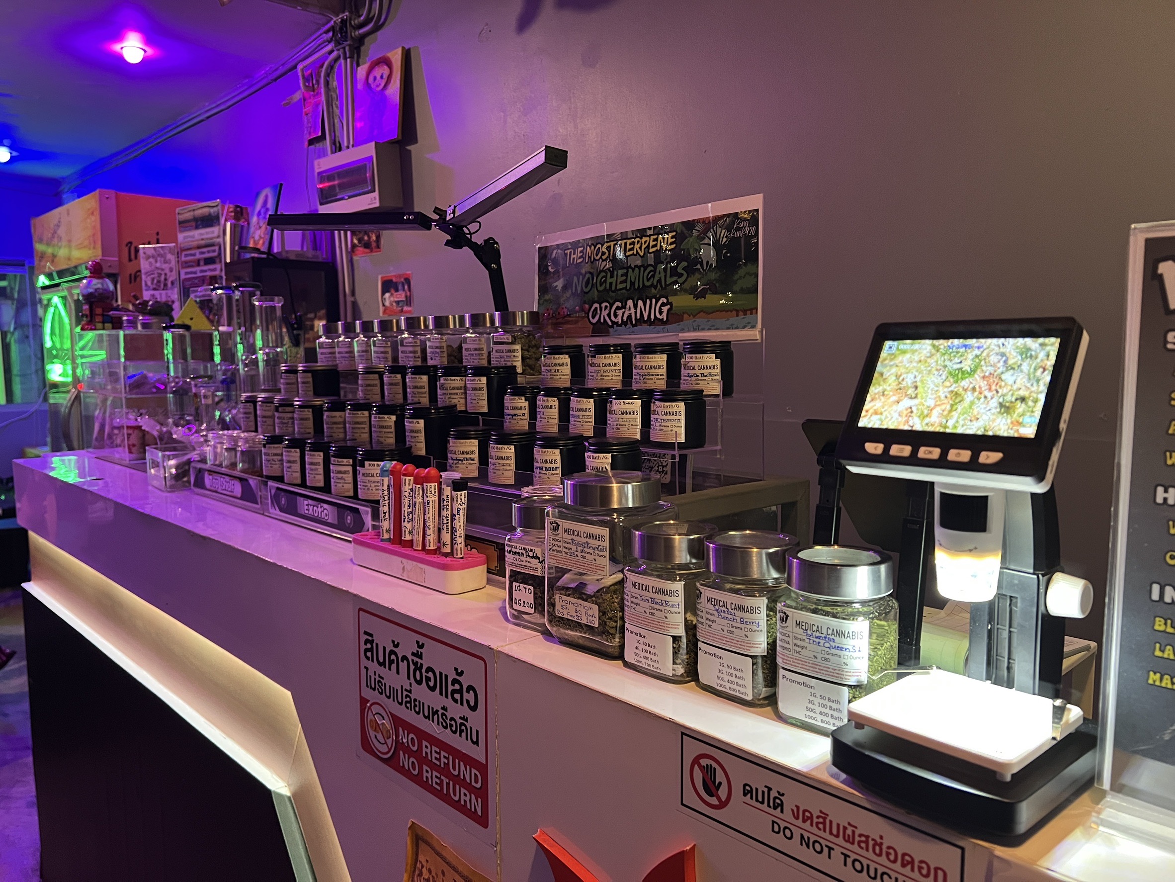เคาน์เตอร์ร้านกัญชาทางการแพทย์ในประเทศไทย มีขวดโหลกัญชาเรียงรายบนชั้นวาง พร้อมเครื่องชั่งดิจิทัลและป้ายไม่รับคืนสินค้า