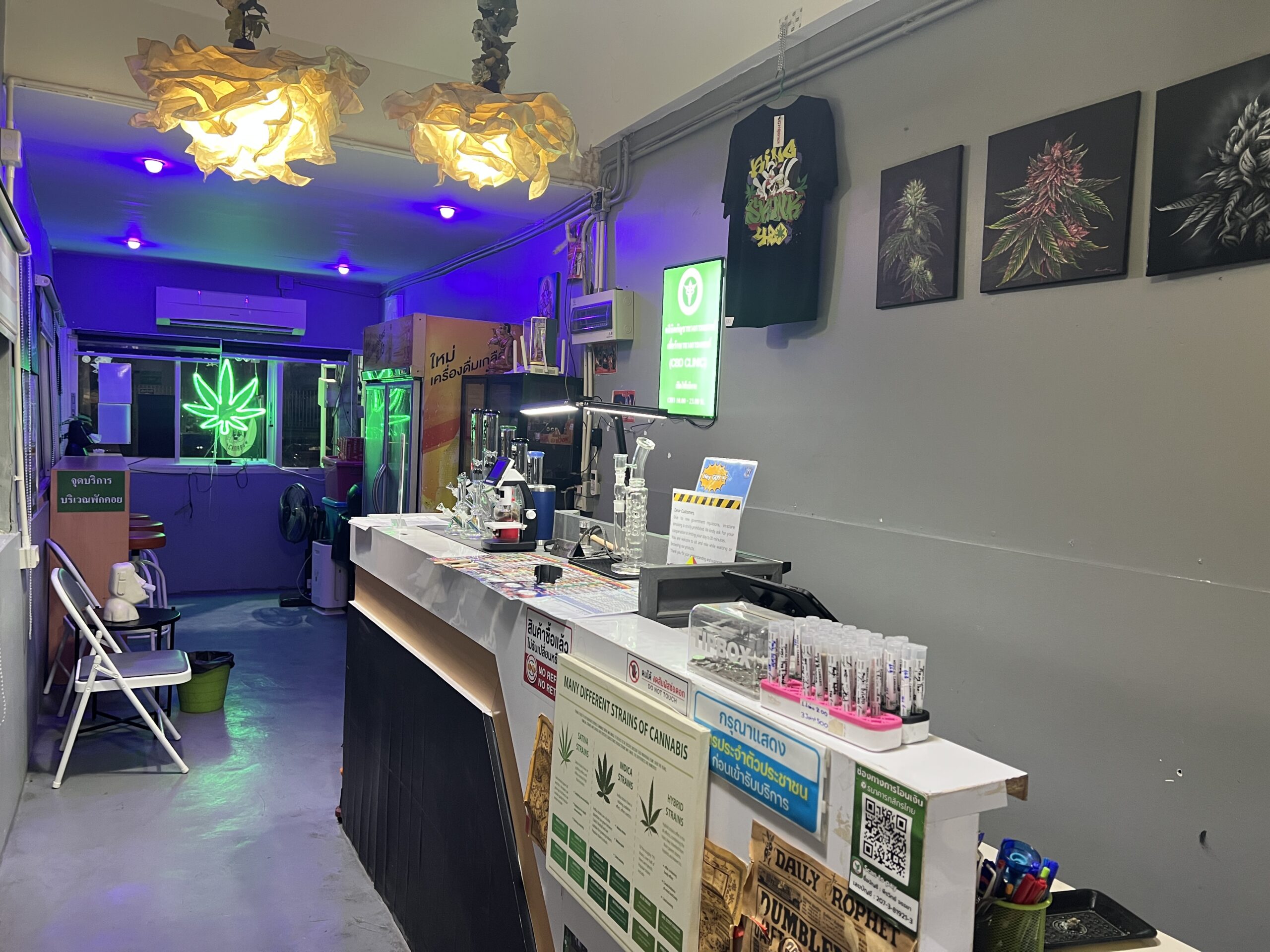 ภายในร้านจำหน่ายกัญชาในประเทศไทย มีเคาน์เตอร์บริการ ไฟนีออนรูปใบกัญชา ภาพวาดใบกัญชาบนผนัง และอุปกรณ์ต่างๆ