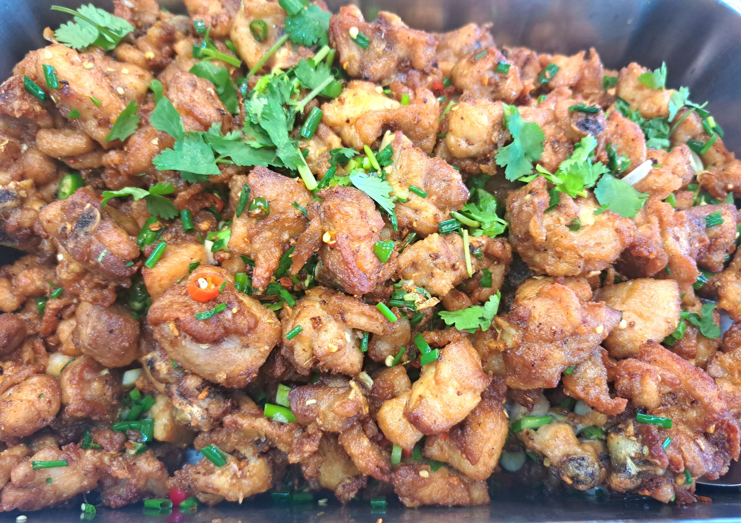 ไก่ทอดเกลือพริกสมุนไพรโรยผักชีและพริกสดบนจานดำ