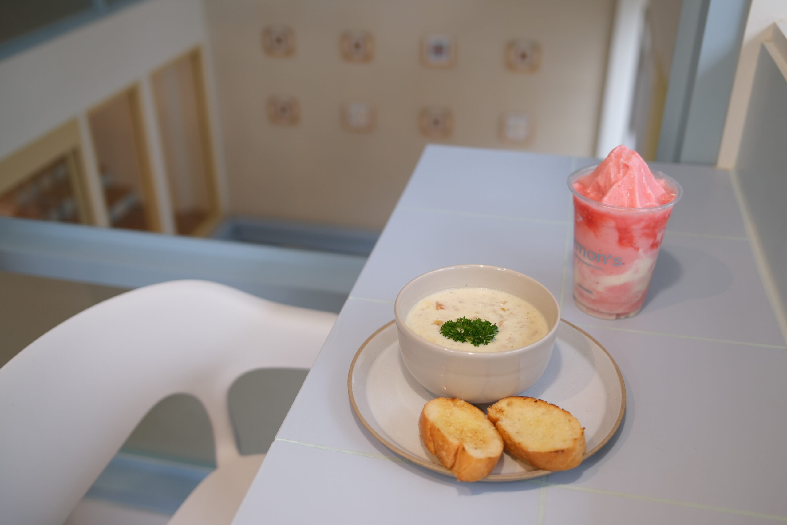 ซุปครีมในชามขาวเสิร์ฟพร้อมขนมปังกระเทียมปิ้งและเครื่องดื่มสมูทตี้สีชมพูบนโต๊ะสีขาวในร้านอาหารสไตล์น่ารัก