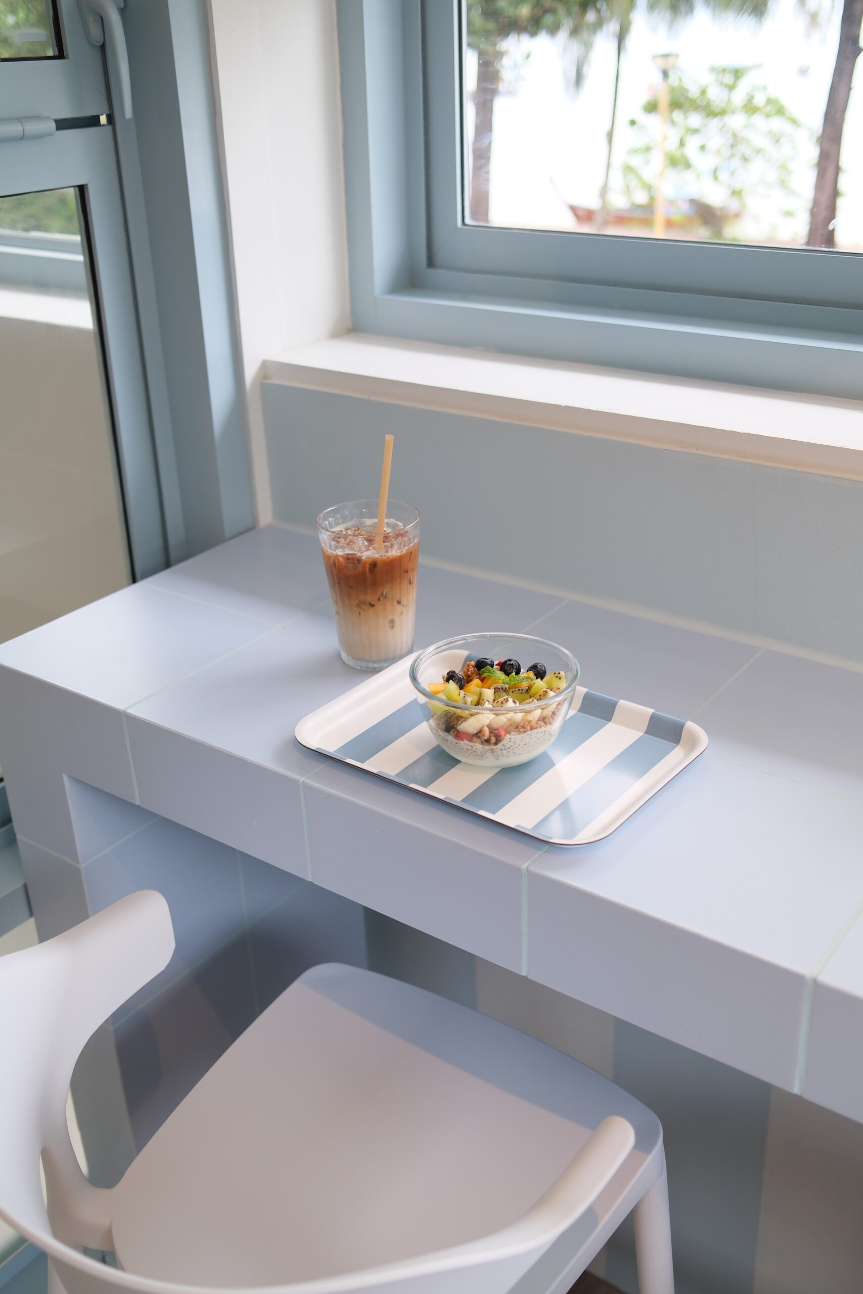 กาแฟเย็นและชามอาซาอีโบว์ลผลไม้สดบนเคาน์เตอร์กระเบื้องสีฟ้าอ่อนในคาเฟ่สไตล์มินิมอล