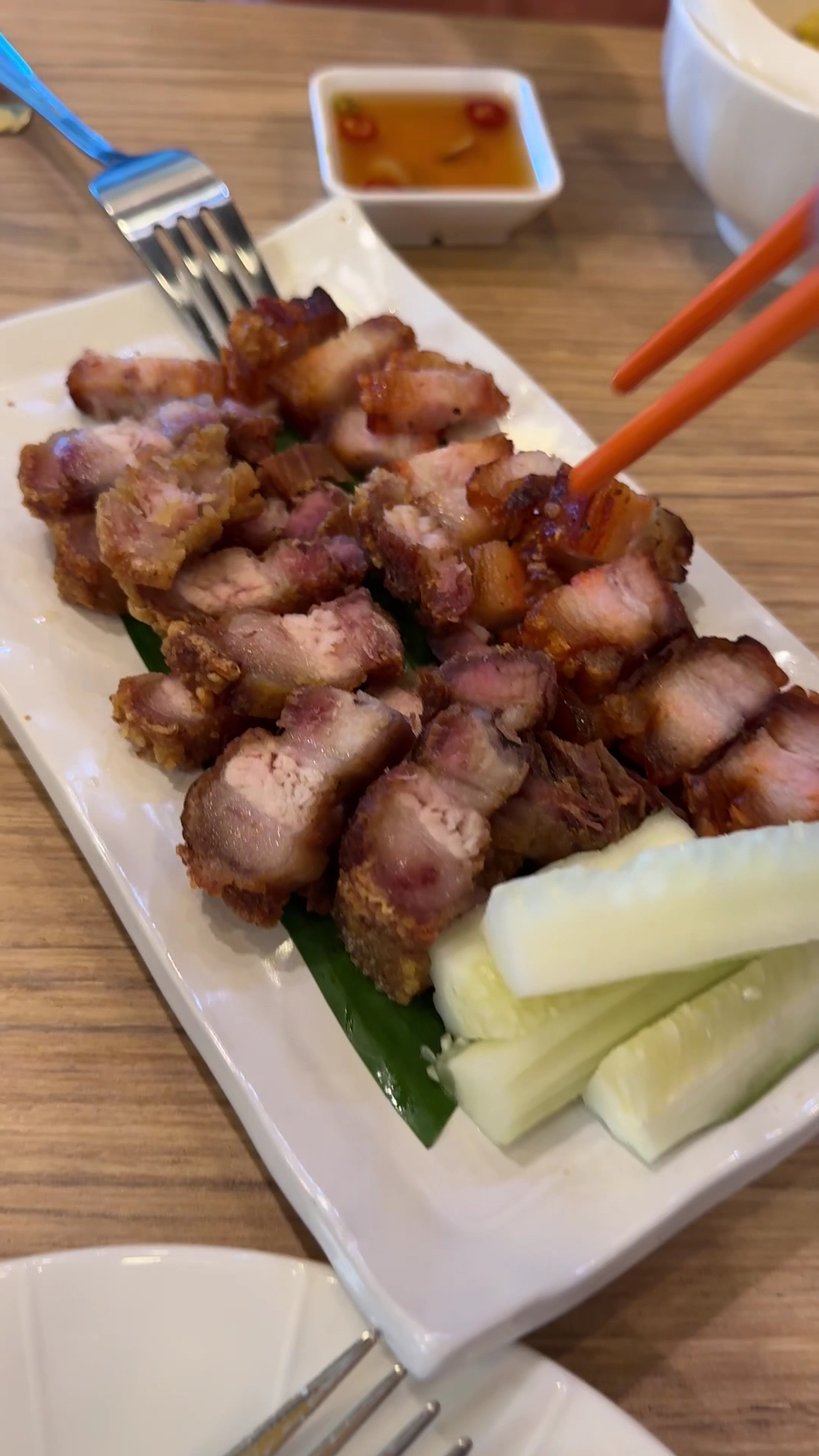 หมูกรอบทอดหั่นชิ้นเสิร์ฟบนจานสี่เหลี่ยมพร้อมแตงกวาหั่นแท่งและน้ำจิ้มพริก