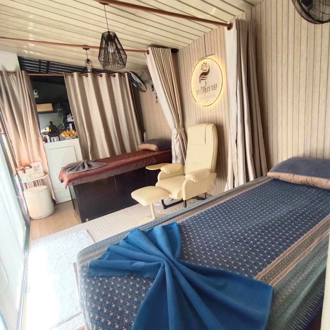 ภายในร้านนวดไทย มีเตียงนวด เก้าอี้นวดสีครีม และป้ายชื่อร้านนกจิกาย พร้อมผ้าม่านกั้นห้อง