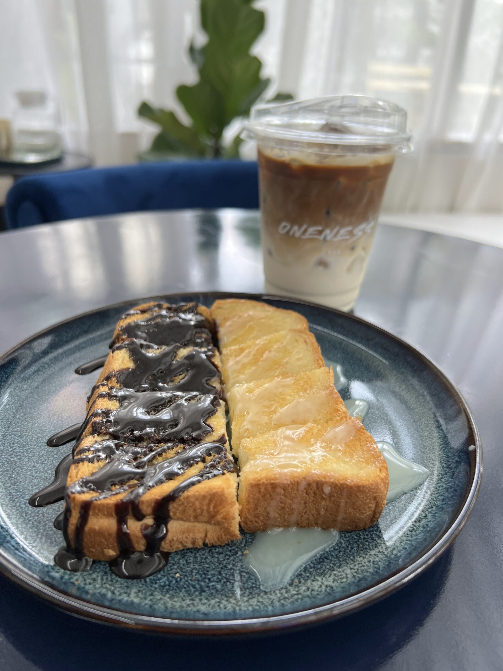 ขนมปังปิ้งราดช็อกโกแลตและน้ำผึ้งเสิร์ฟคู่กับกาแฟเย็นร้าน Oneness บนจานสีน้ำเงิน