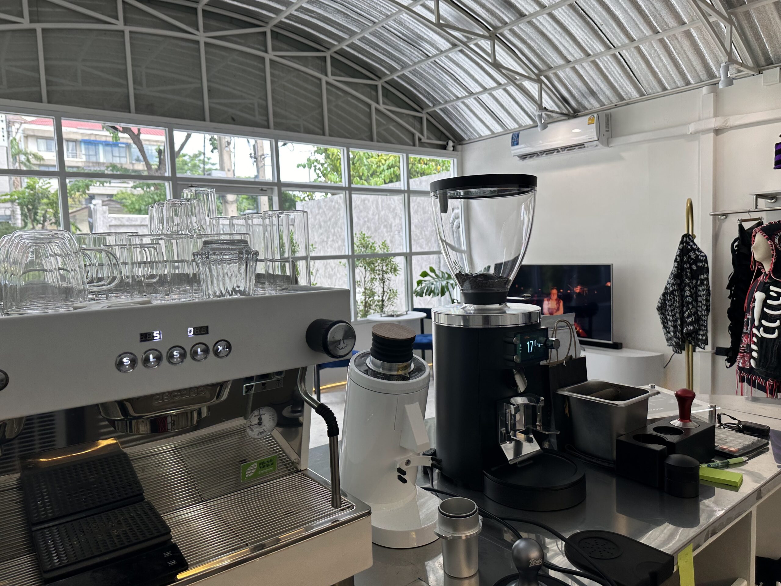 เคาน์เตอร์บาร์กาแฟพร้อมเครื่องชงเอสเปรสโซสีขาวและเครื่องบดกาแฟในร้านกาแฟหลังคาโค้งกระจกใส