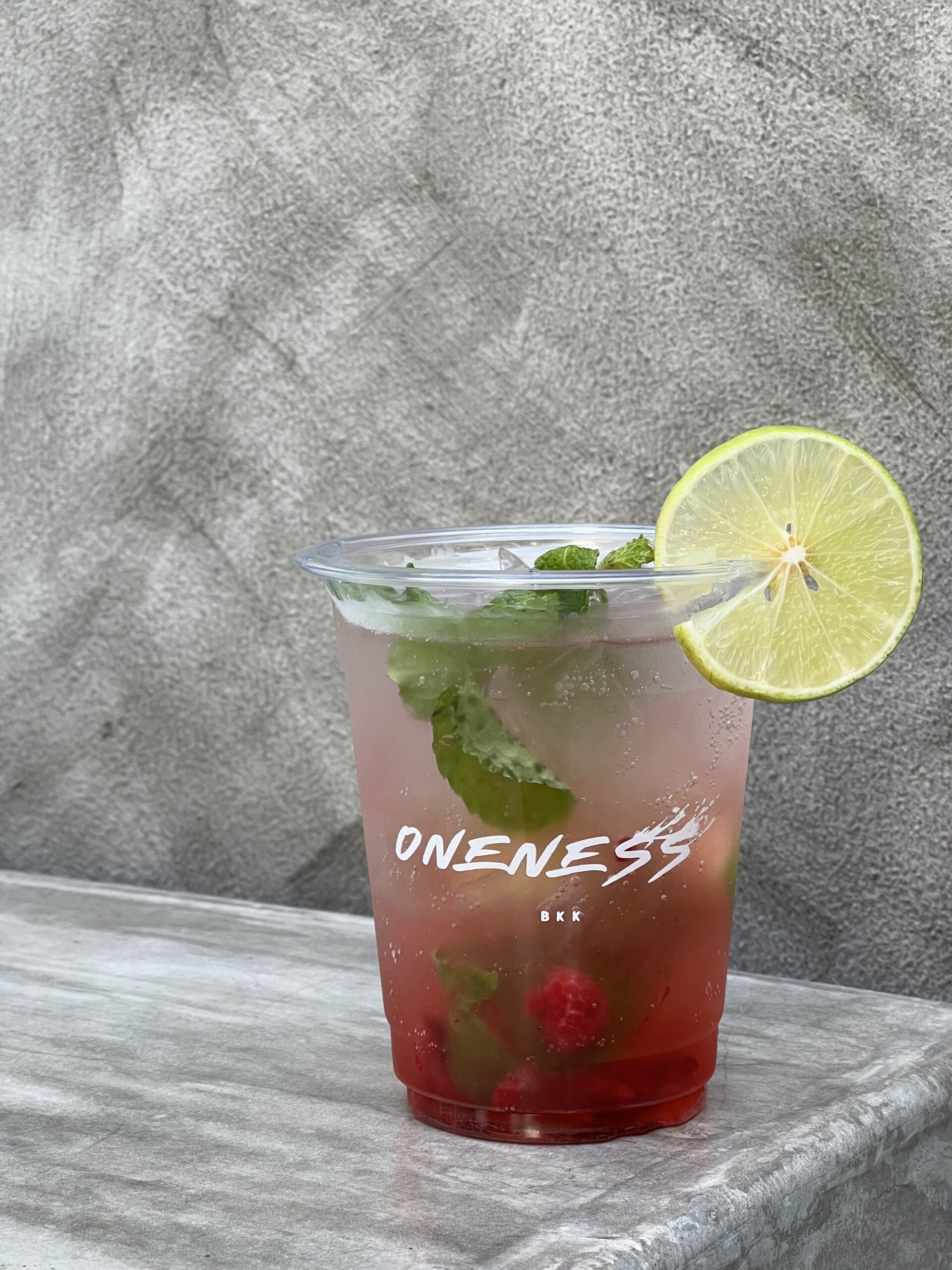 เครื่องดื่มม็อกเทลราสเบอร์รี่โมฮิโตพร้อมใบสะระแหน่และมะนาวในแก้วพลาสติกจากร้าน Oneness BKK