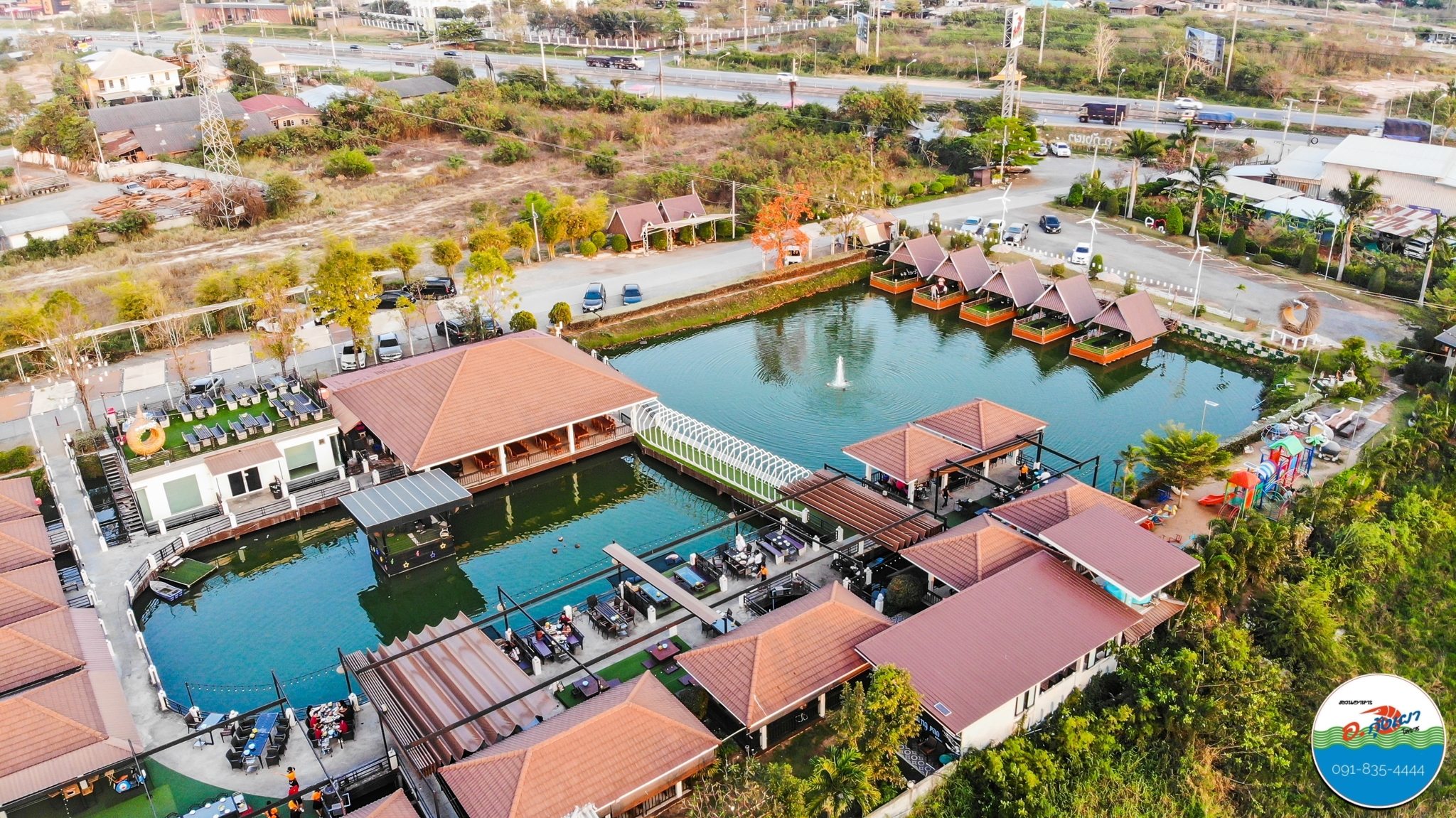 ภาพมุมสูงของร้านอาหารริมน้ำพร้อมศาลาลอยน้ำหลังคาสีน้ำตาลแดง สระว่ายน้ำ และทะเลสาบขนาดใหญ่ บรรยากาศสวยงาม