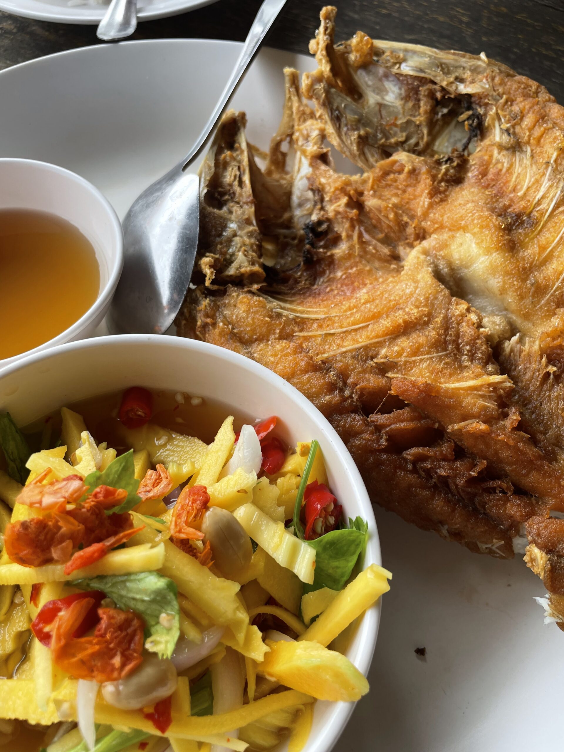 ปลาทอดกรอบเสิร์ฟพร้อมยำมะม่วงและน้ำจิ้ม บนจานขาว