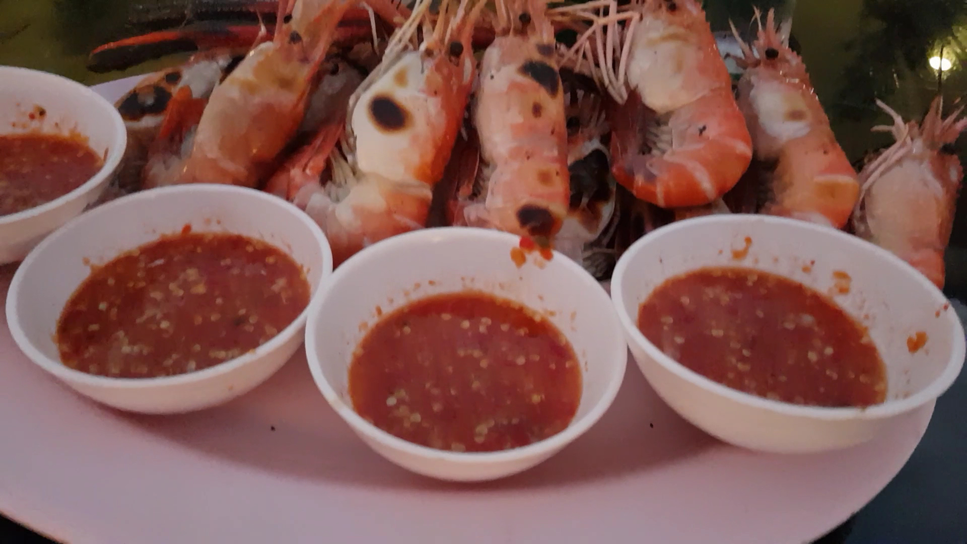 กุ้งเผาตัวใหญ่เสิร์ฟพร้อมน้ำจิ้มซีฟู้ดในถ้วยขาว 4 ถ้วย บนจานสีชมพู