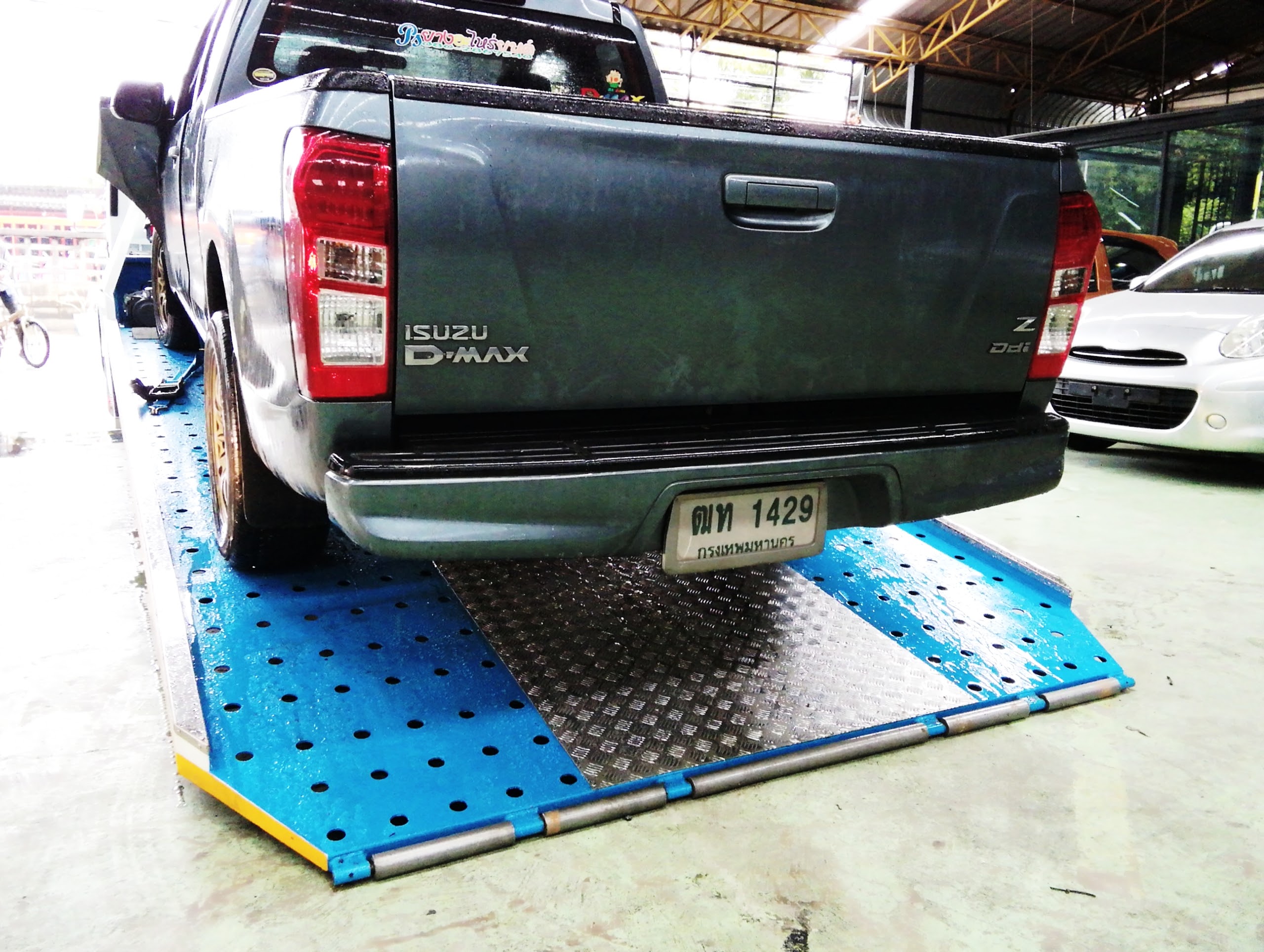 รถกระบะอีซูซุดีแมกซ์สีเทาเข้มจอดอยู่บนแท่นยกรถในอู่ซ่อมรถ