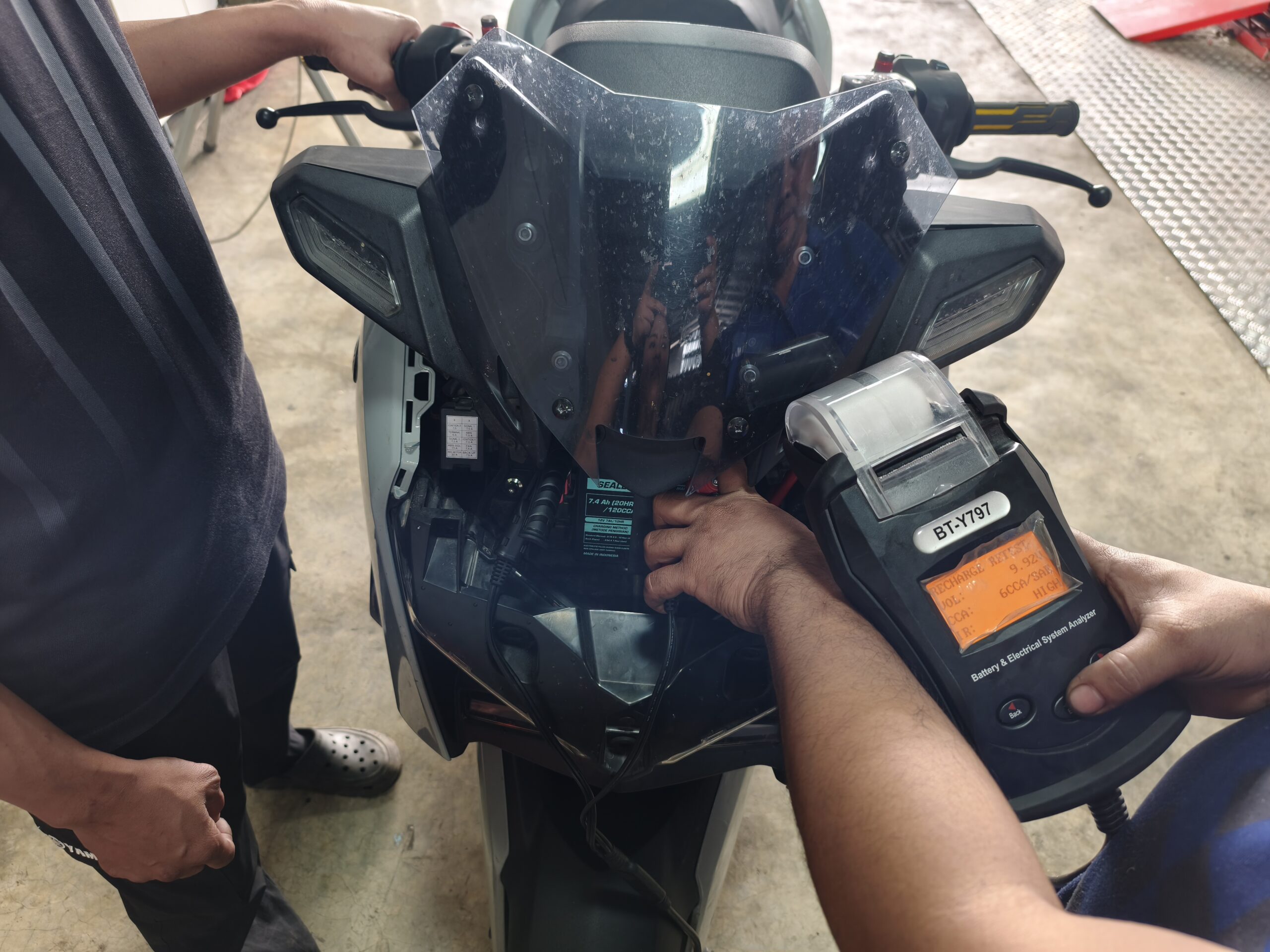 ช่างกำลังตรวจสอบแบตเตอรี่รถมอเตอร์ไซค์ด้วยเครื่องวิเคราะห์ระบบไฟฟ้า BT-Y797 ในอู่ซ่อมรถ