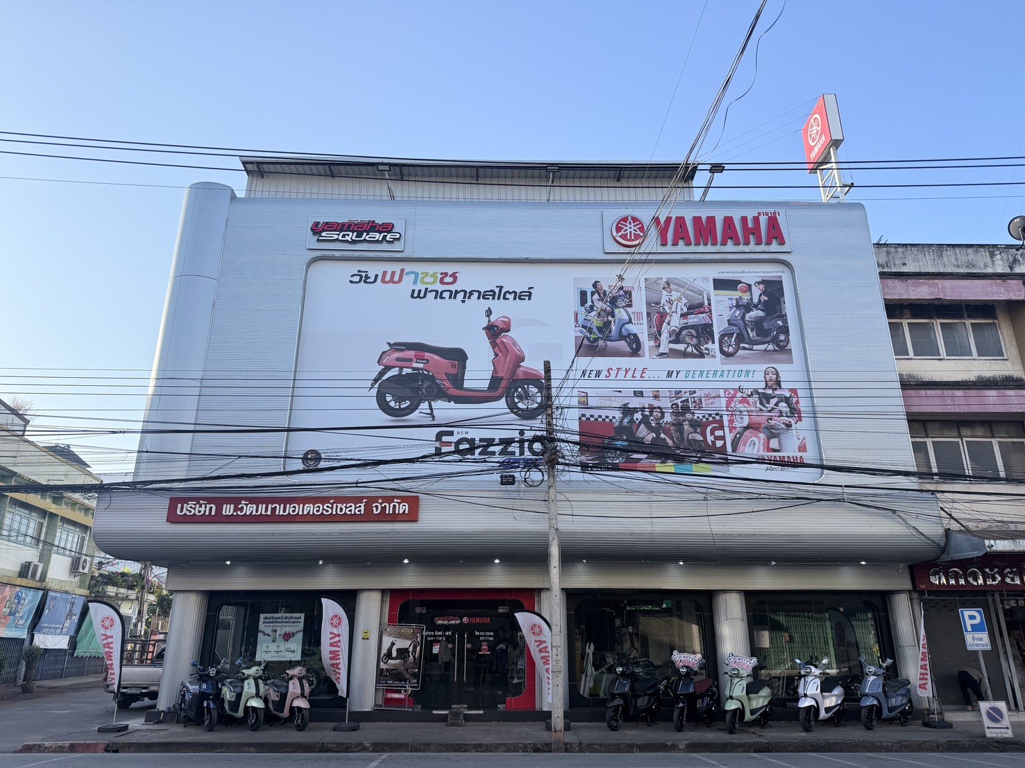 ร้านยามาฮ่าสแควร์ ตัวแทนจำหน่ายรถจักรยานยนต์ยามาฮ่า มีป้ายโฆษณารถ Fazzio สีชมพูขนาดใหญ่บนอาคาร พร้อมรถมอเตอร์ไซค์จอดหน้าร้าน