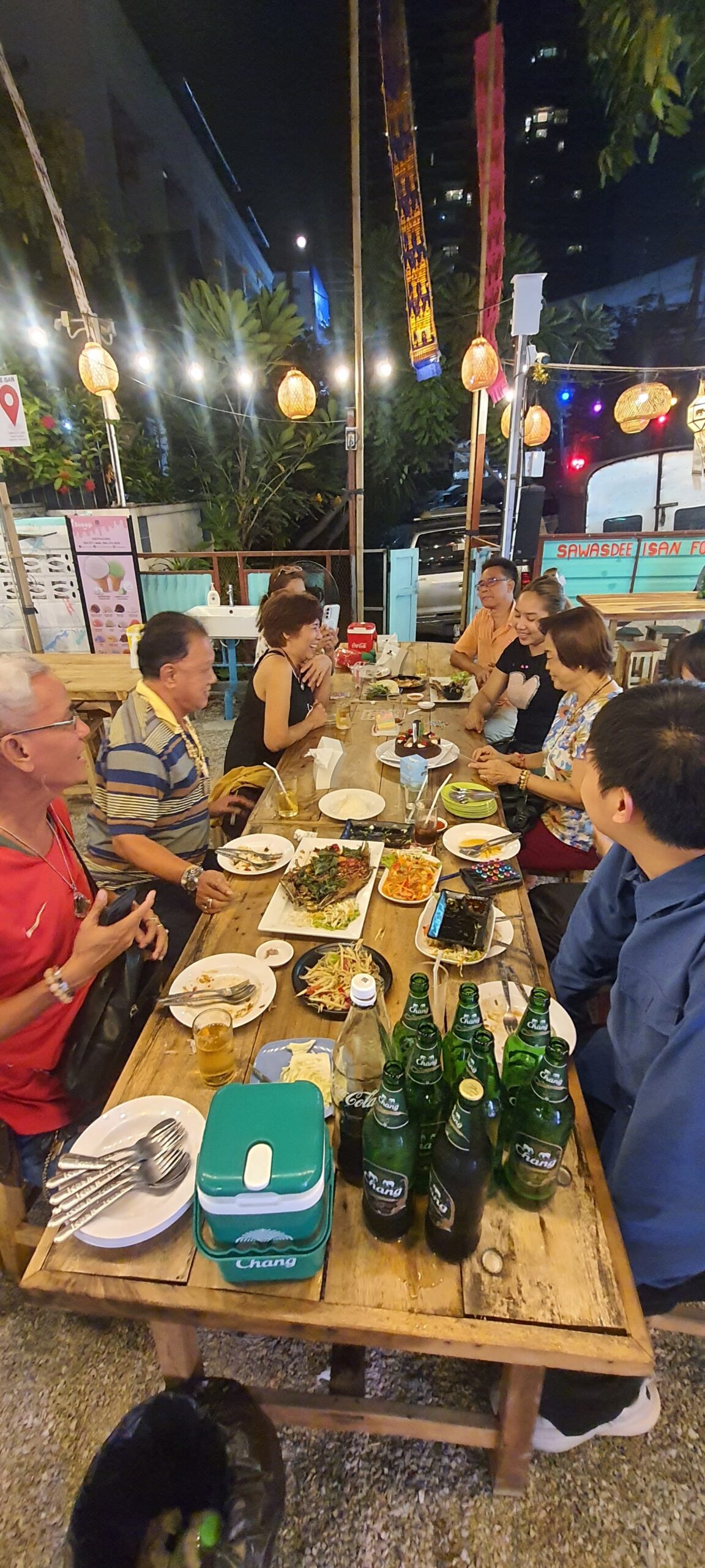 กลุ่มเพื่อนนั่งรับประทานอาหารอีสานพร้อมเบียร์ช้างที่ร้านสวัสดีอีสานฟู้ดในบรรยากาศกลางแจ้งยามค่ำคืน