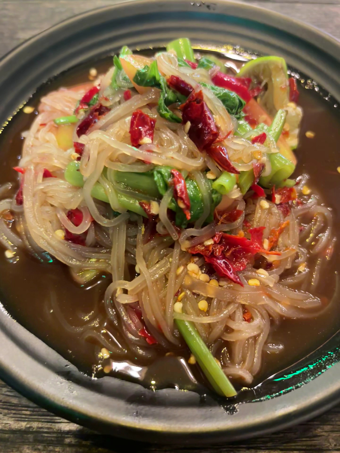 วุ้นเส้นผัดพริกแห้งในชามดำ มีผักบุ้งและพริกแห้งเม็ดพริกโรยหน้า น้ำซุปรสจัด