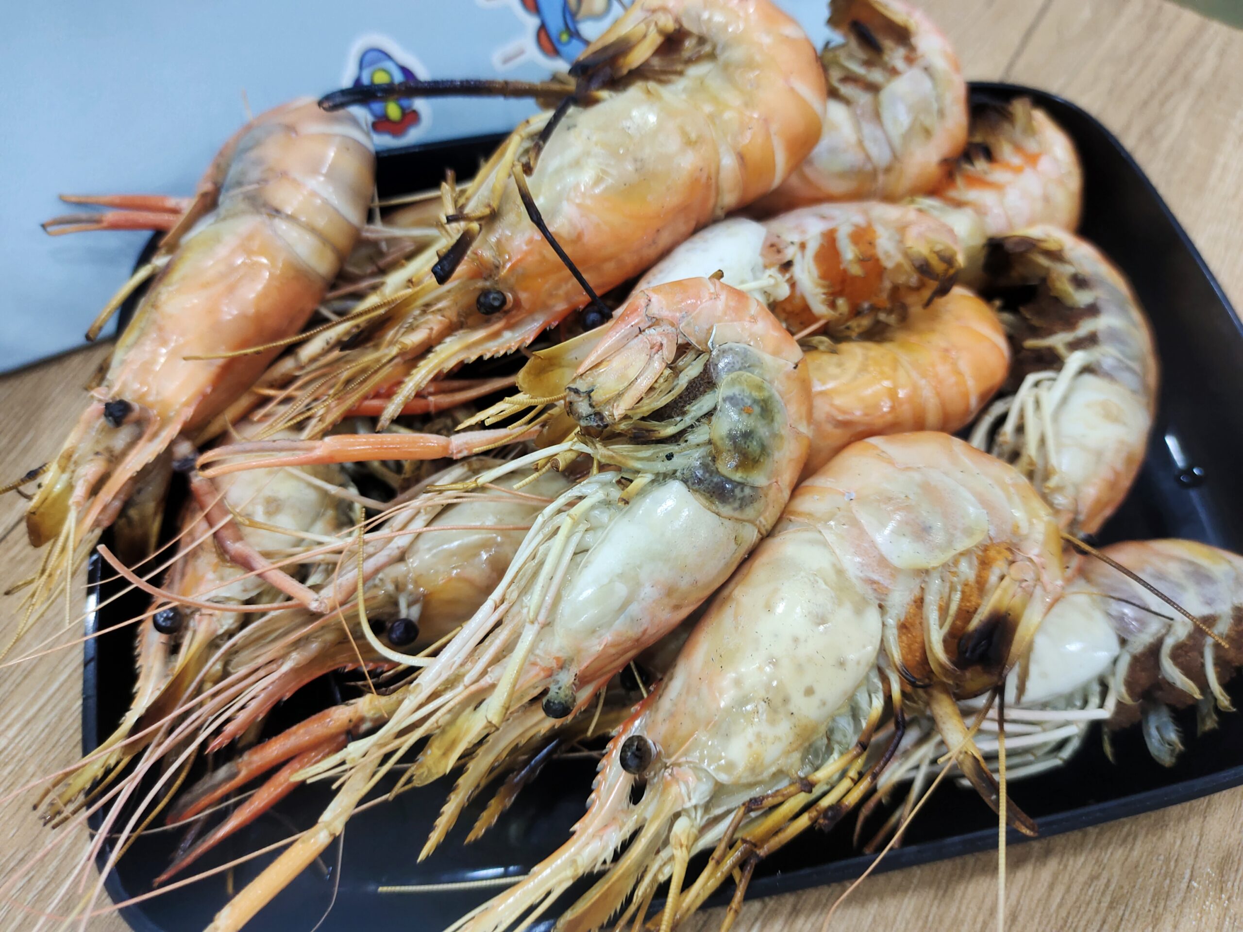 กุ้งแม่น้ำย่างสุกจัดเรียงบนจานสีดำ เนื้อกุ้งสีส้มอวบใหญ่พร้อมหัวกุ้งมันเยิ้ม