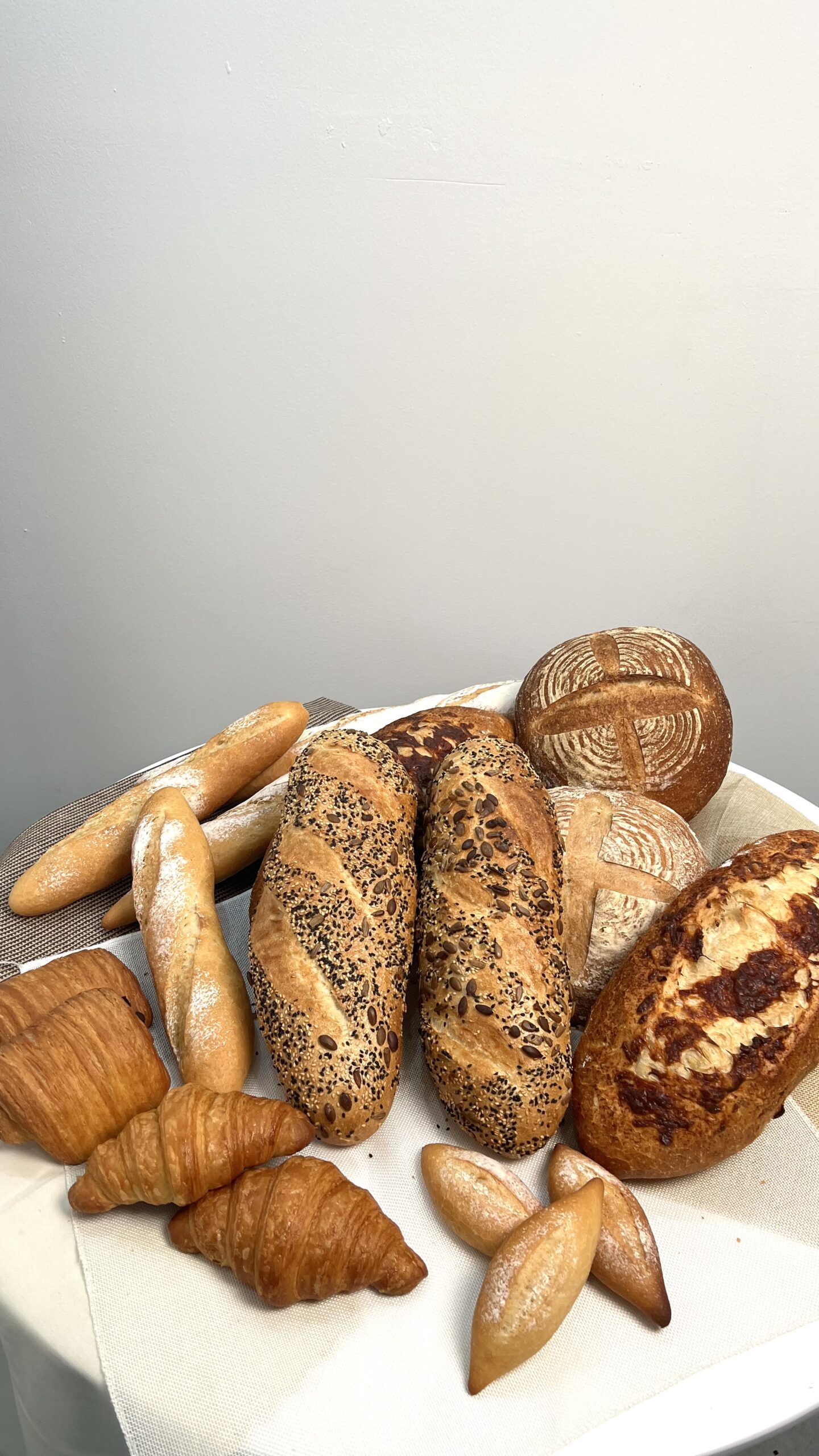 การจัดแสดงขนมปังหลากหลายชนิด ได้แก่ ครัวซองต์ บาแก็ต ขนมปังธัญพืช และขนมปังซาวร์โดว์บนโต๊ะสีขาว