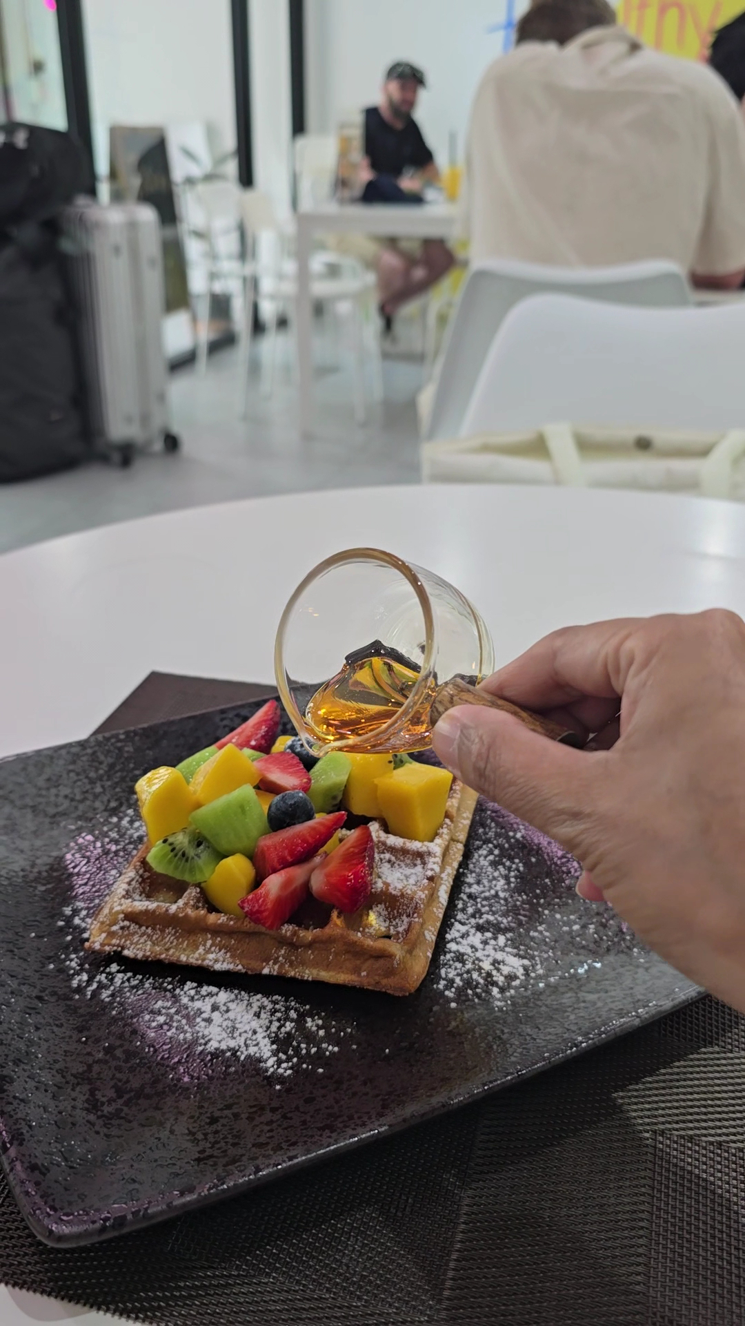 วาฟเฟิลท็อปปิ้งผลไม้สดราดน้ำผึ้งบนจานสีดำโรยผงน้ำตาล