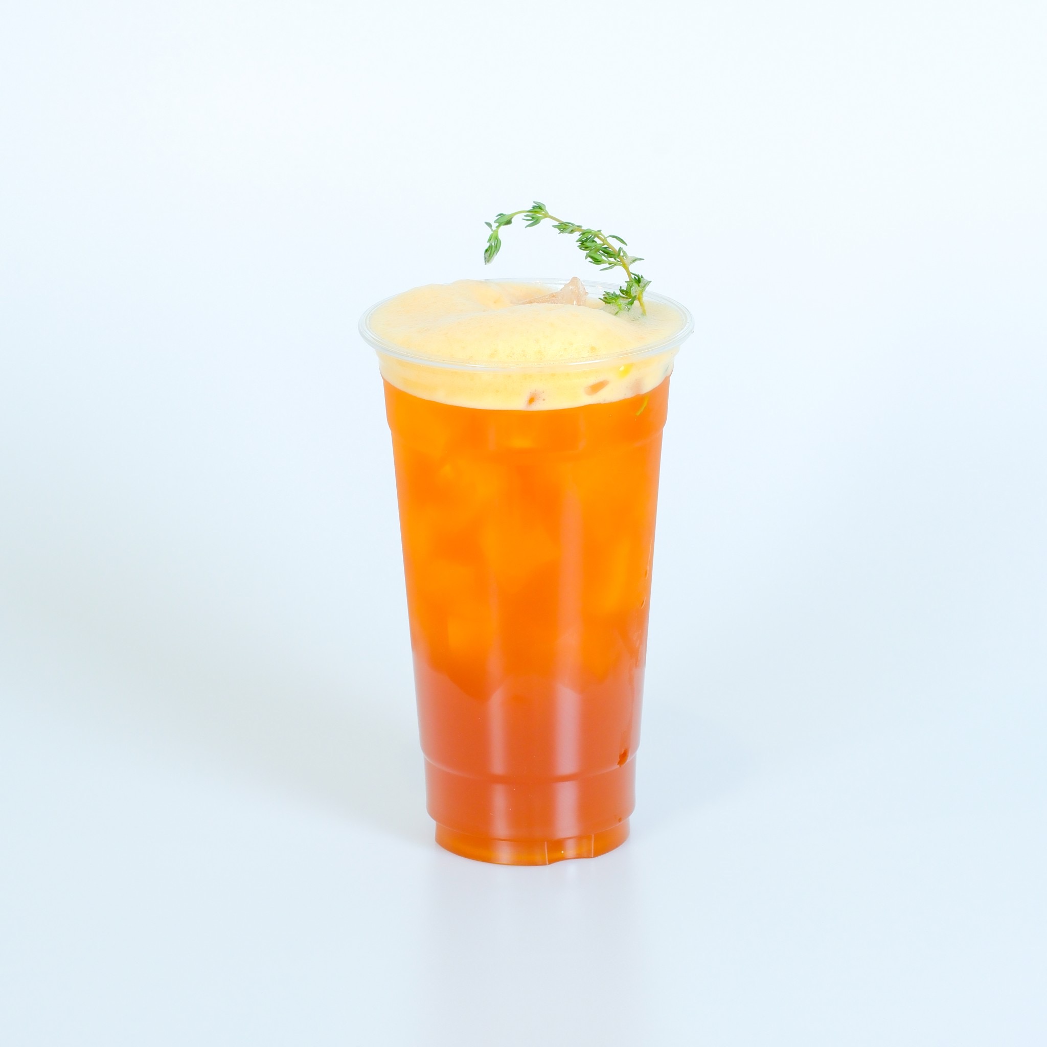 ชาเย็นสีส้มในแก้วพลาสติกใสราดด้วยครีมชีสโฟมตกแต่งด้วยใบไธม์สด