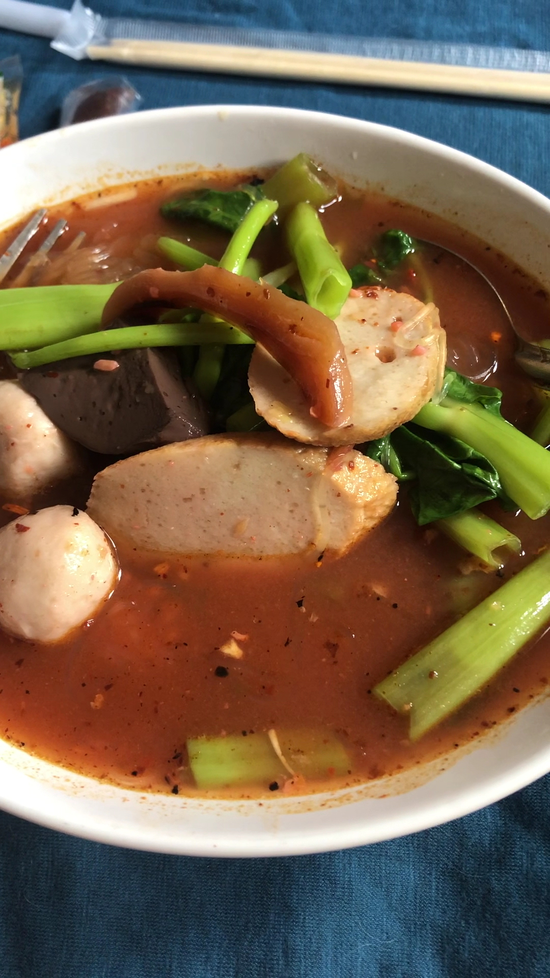 ก๋วยเตี๋ยวเรือน้ำตกใส่ลูกชิ้น เนื้อสับ ผักคะน้า และเครื่องในในชามสีขาว