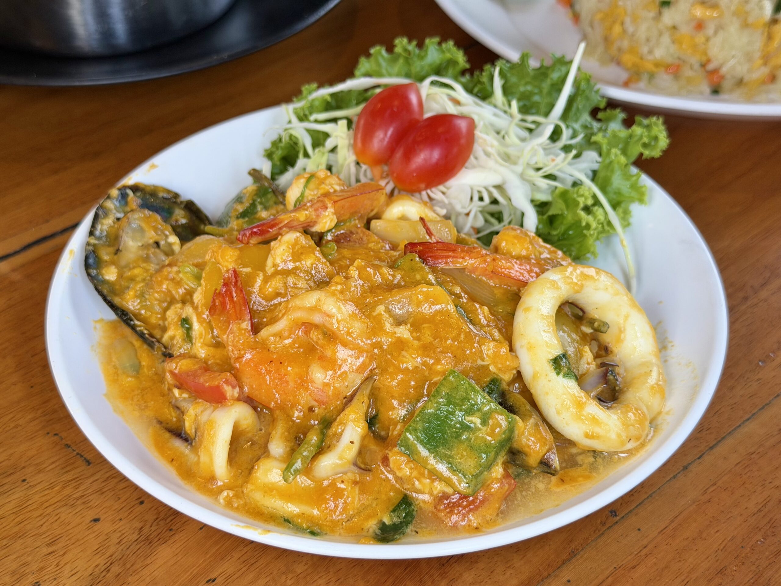 จานอาหารทะเลผัดผงกะหรี่รวมมิตร มีกุ้ง หมึก หอยแมลงภู่ และผักในซอสสีเหลืองเข้มข้น เสิร์ฟพร้อมผักสดและมะเขือเทศราชินี