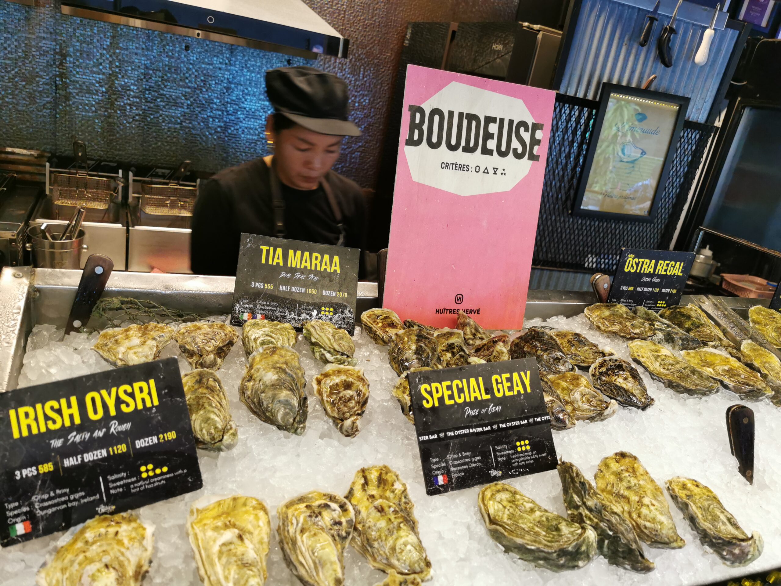 บาร์หอยนางรมสดบนน้ำแข็งหลายชนิด ได้แก่ Irish Oysri, Tia Maraa, Special Geay และ Ostra Regal พร้อมป้ายราคาและป้าย Boudeuse จาก Huîtres Hervé