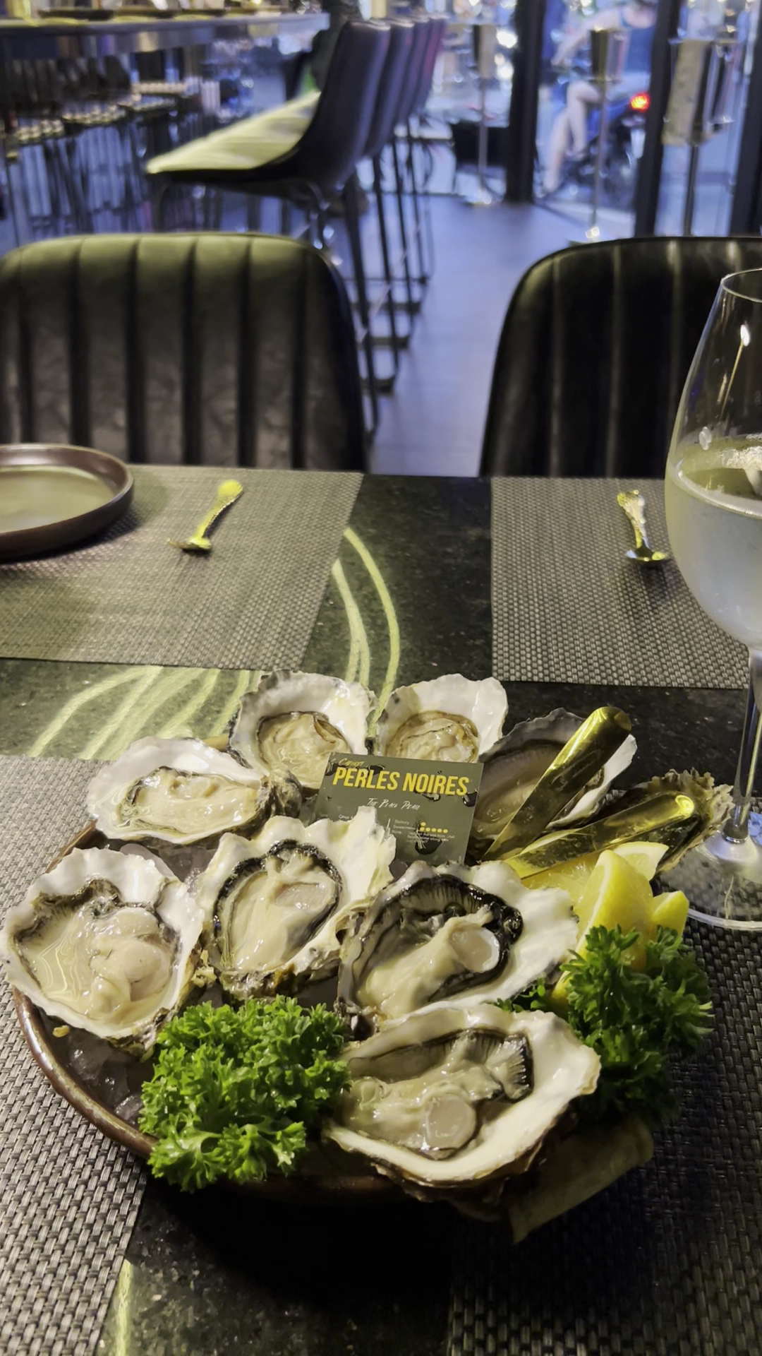 จานหอยนางรมสดเสิร์ฟบนจานพร้อมผักชีฝรั่งและมะนาว แบรนด์ Perles Noires พร้อมไวน์ขาวในร้านอาหารบรรยากาศหรูหรา