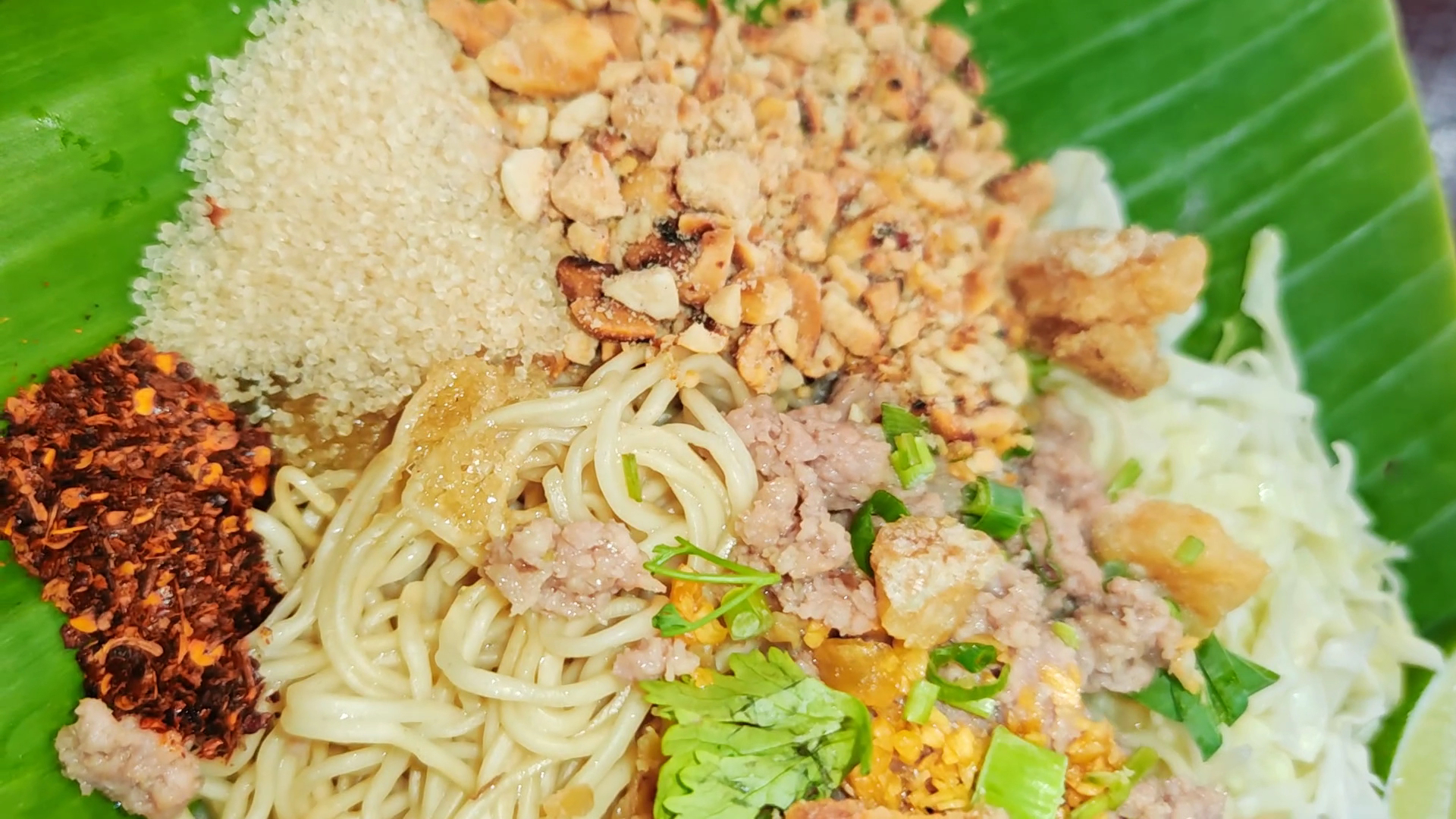บะหมี่แห้งบนใบตอง โรยหมูสับ กากหมู ถั่วลิสง พริกป่น งาขาว ผักชี มะนาว