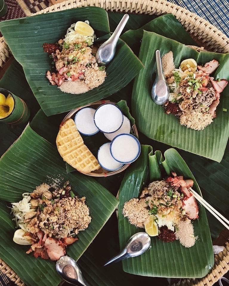 อาหารไทยบนใบตองเสิร์ฟบนถาดจักสานพร้อมข้าวคั่ว เนื้อย่าง มะนาว และขนมปังกรอบกับเครื่องดื่ม