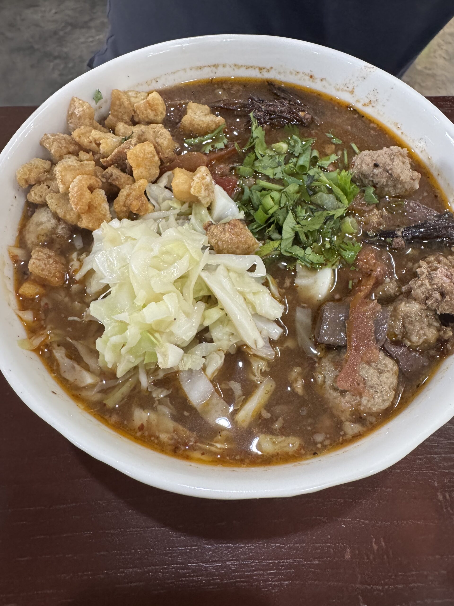 ก๋วยเตี๋ยวน้ำเงี้ยวในชามขาว มีผักกาดดอง ผักชี แคบหมู เลือดและเนื้อหมู ในน้ำซุปสีน้ำตาลเข้ม