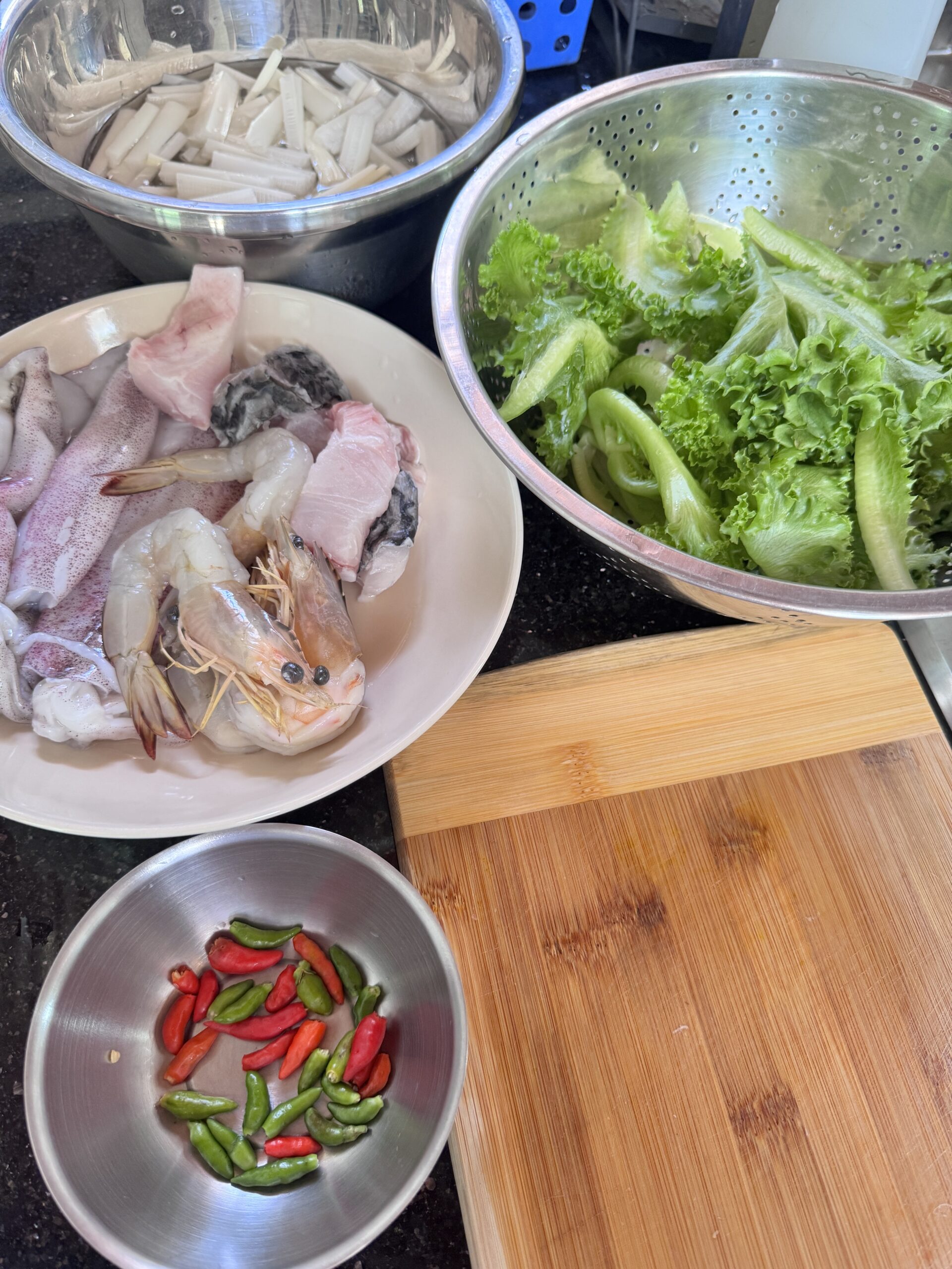 วัตถุดิบสดสำหรับทำอาหารทะเล มีกุ้ง ปลาหมึก ปลา ผักกาดหอม พริกสด และหัวปลีหั่นบนเคาน์เตอร์ครัว