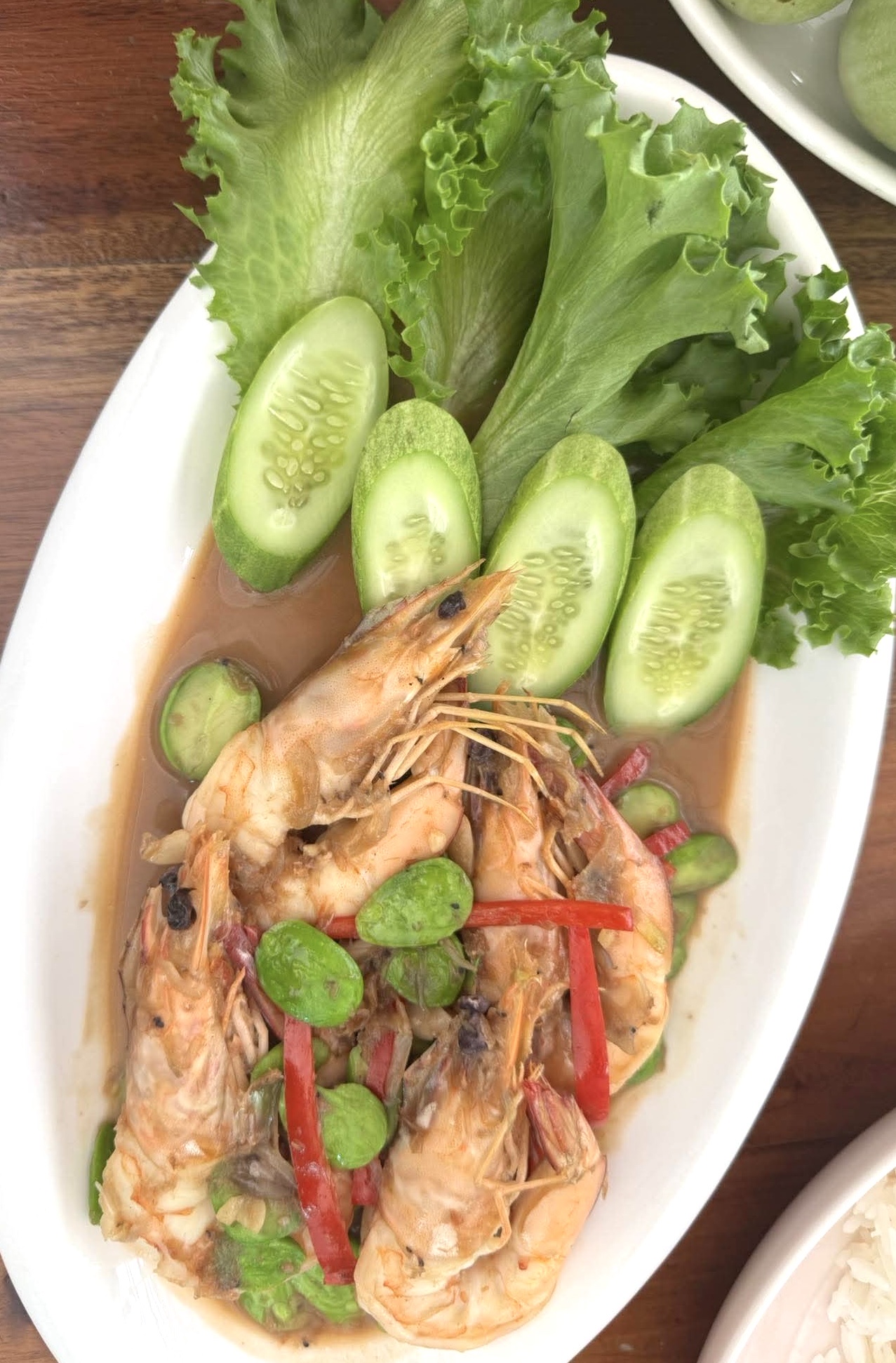 กุ้งผัดสะตอพริกแกง จัดเสิร์ฟบนจานรีพร้อมแตงกวาหั่นและผักกาดหอม